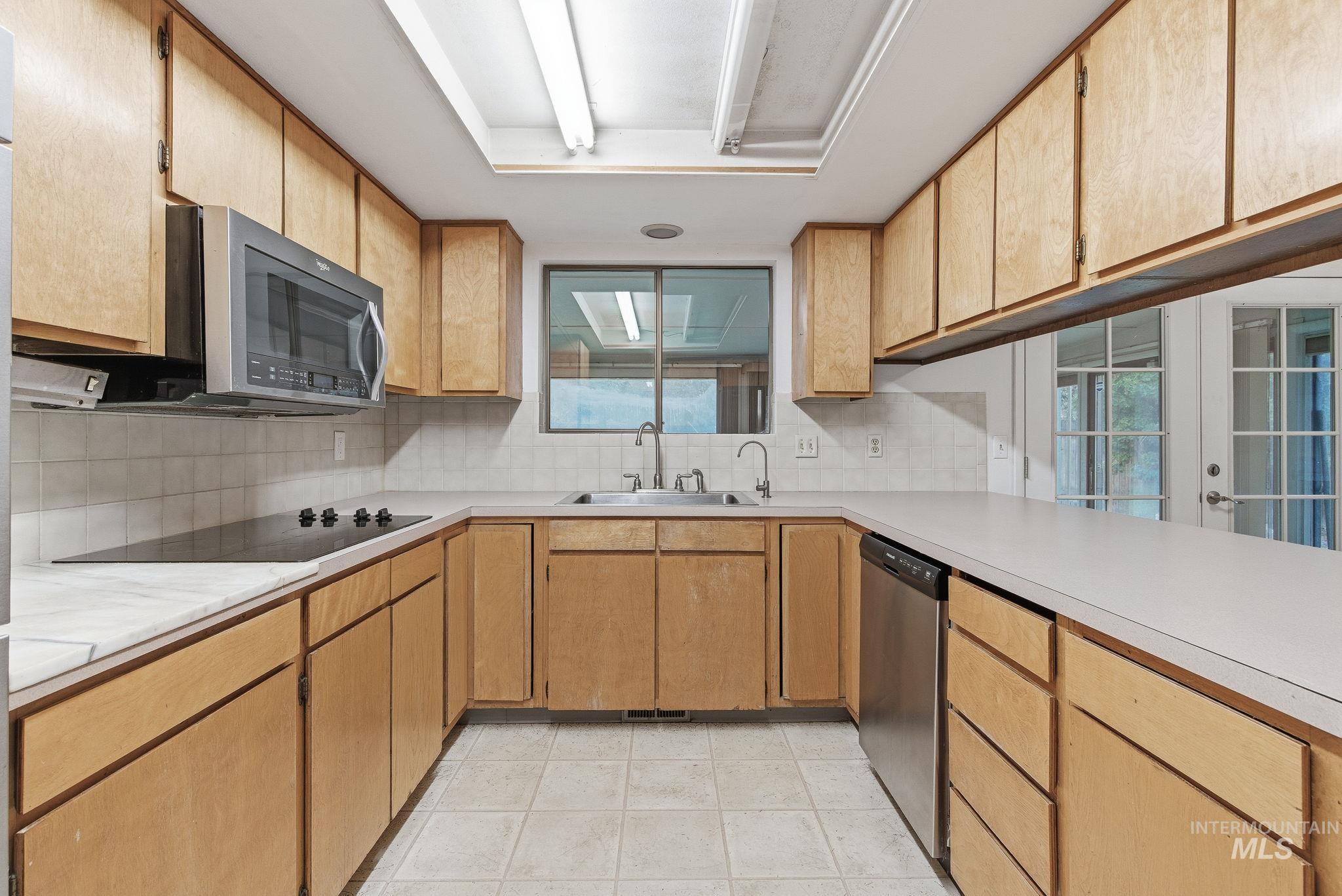 Kitchen with light countertops, decorative backsplash, appliances with stainless steel finishes, and light tile patterned floors