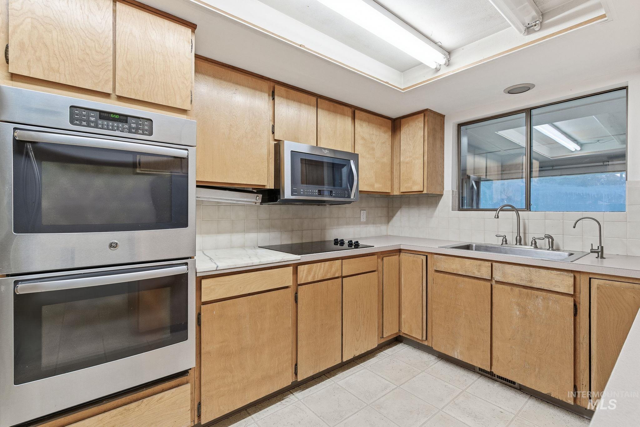 Kitchen featuring appliances with stainless steel finishes, decorative backsplash, light countertops, and light tile patterned flooring