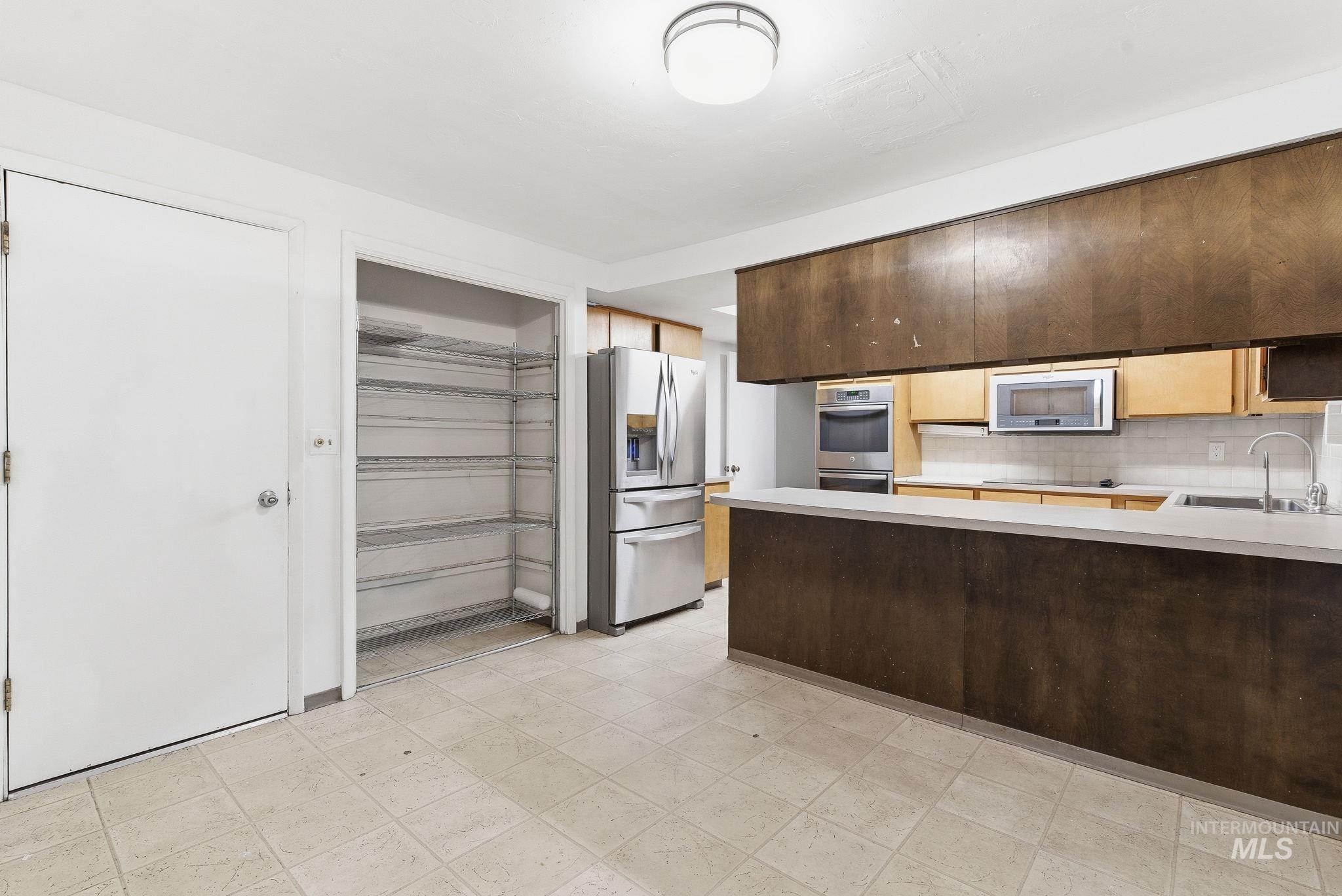 Kitchen with light countertops, stainless steel appliances, a peninsula, backsplash, and light flooring