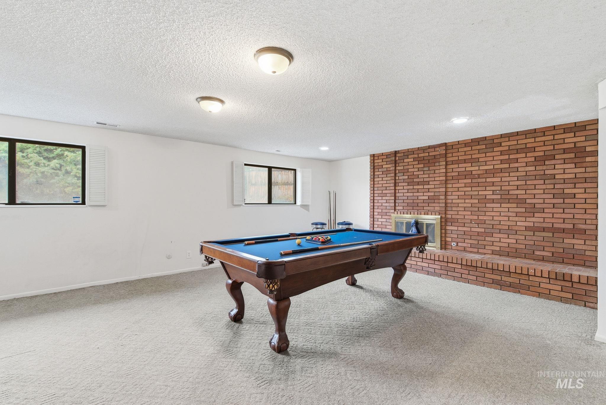 Rec room featuring billiards, carpet, brick wall, and a textured ceiling