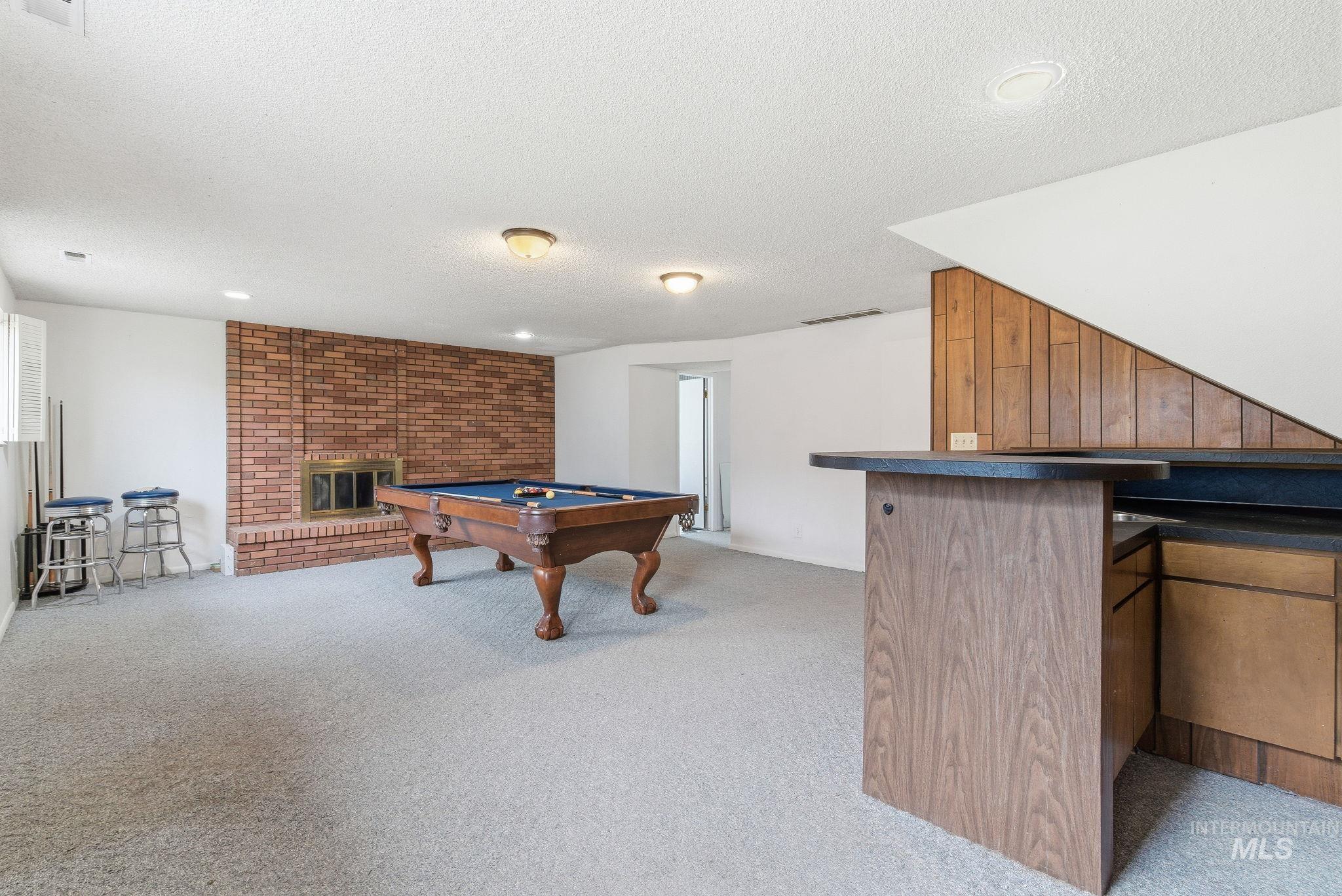 Playroom with billiards, a brick fireplace, light colored carpet, a textured ceiling, and a dry bar