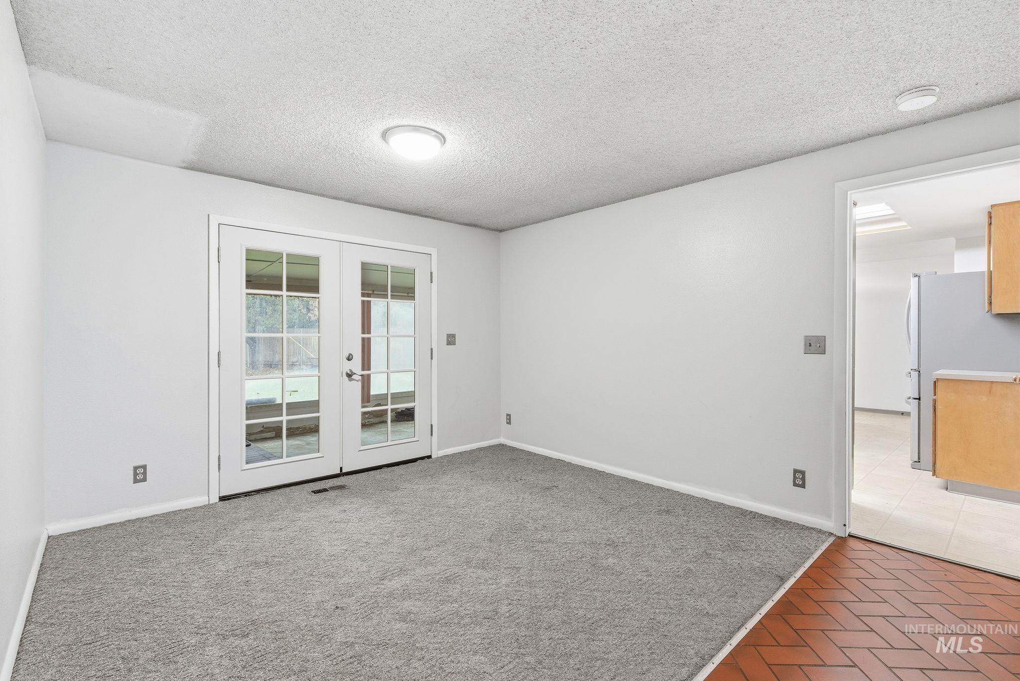 Empty room with a textured ceiling, light carpet, and french doors