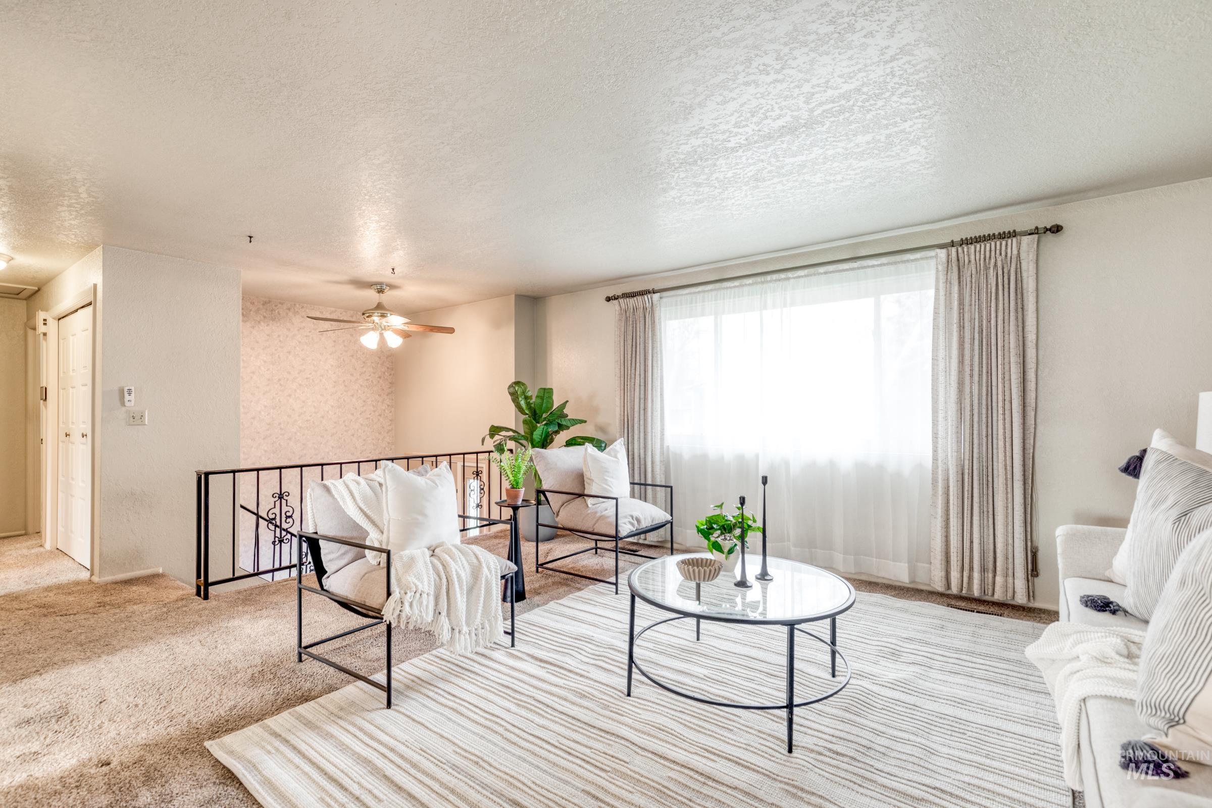 Carpeted living area featuring a textured ceiling, a ceiling fan, and wallpapered walls