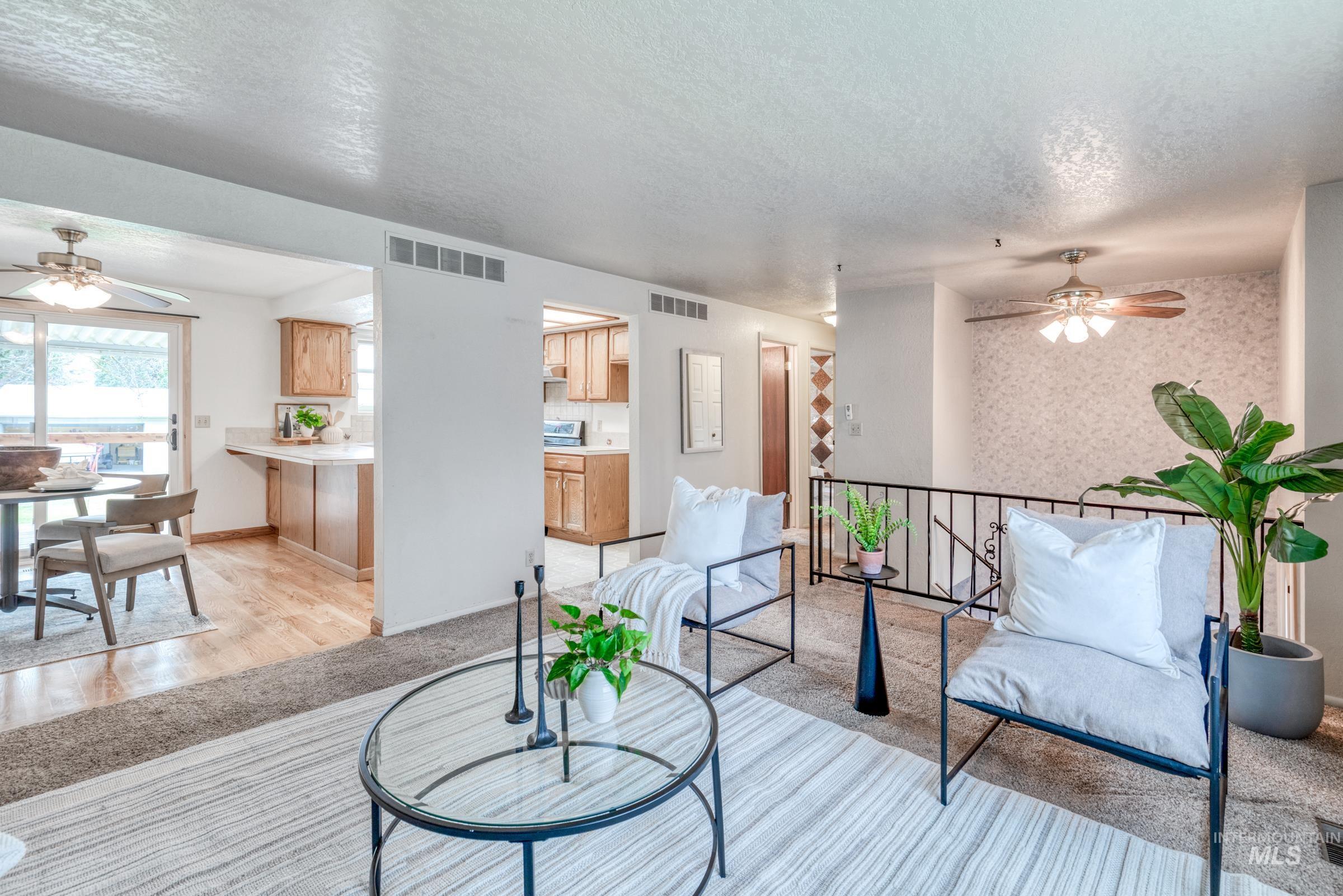 Living room with a ceiling fan, a textured ceiling, wallpapered walls, and light colored carpet