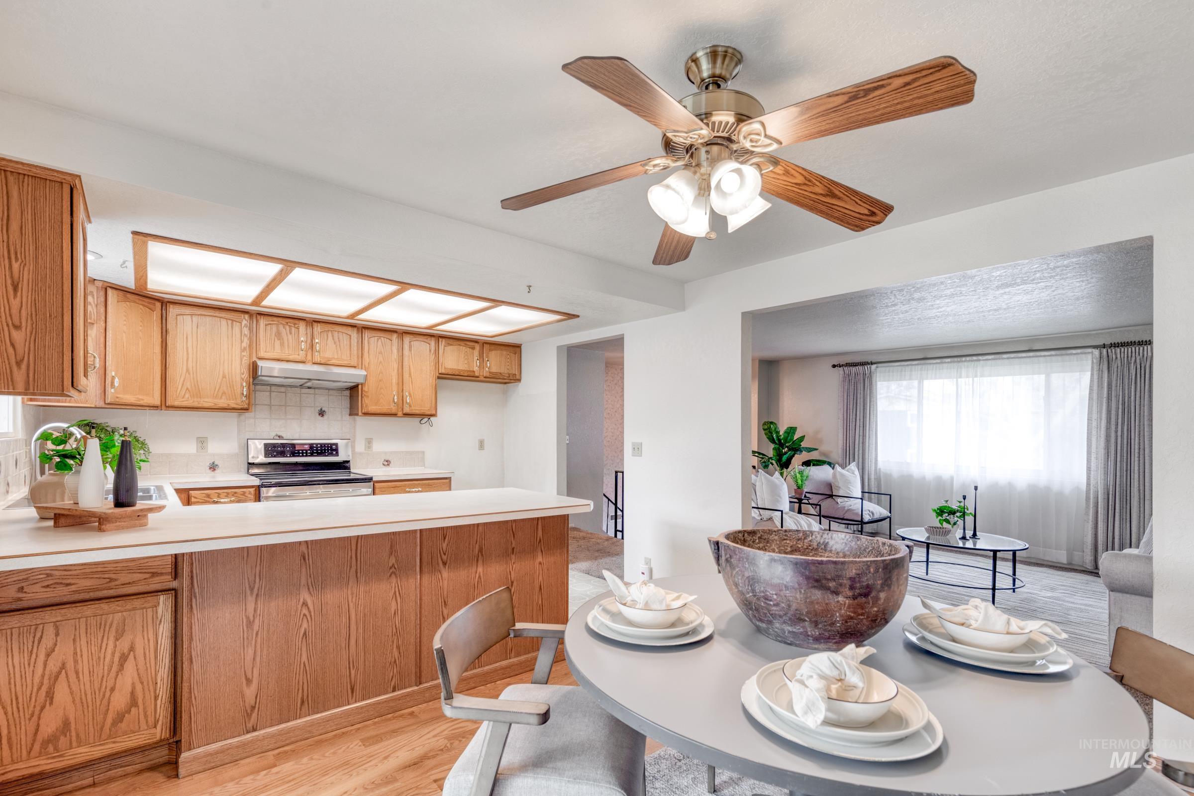 Kitchen featuring light countertops, light wood finished floors, electric range, a peninsula, and a ceiling fan