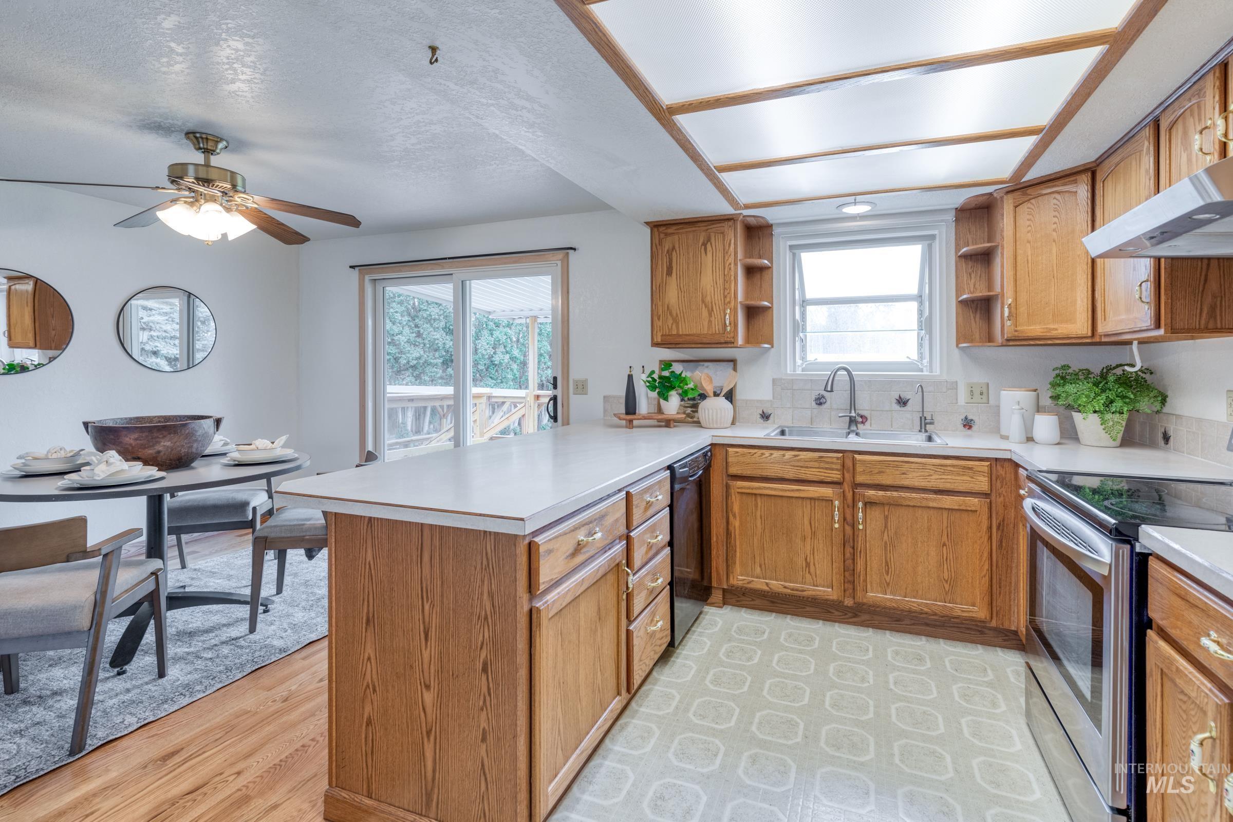 Kitchen with brown cabinets, stainless steel electric range oven, a peninsula, light countertops, and a textured ceiling