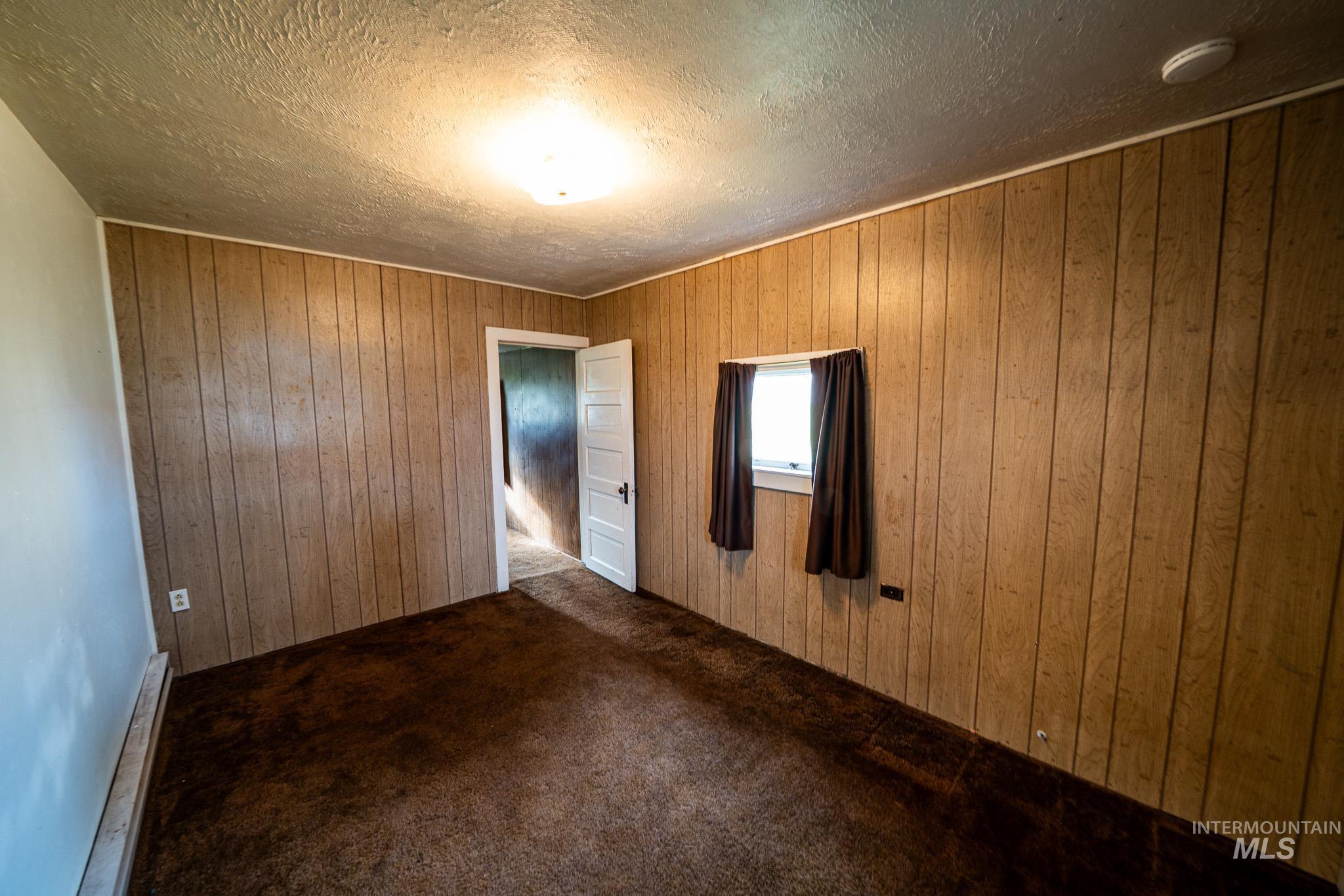 Carpeted empty room with wooden walls and a textured ceiling