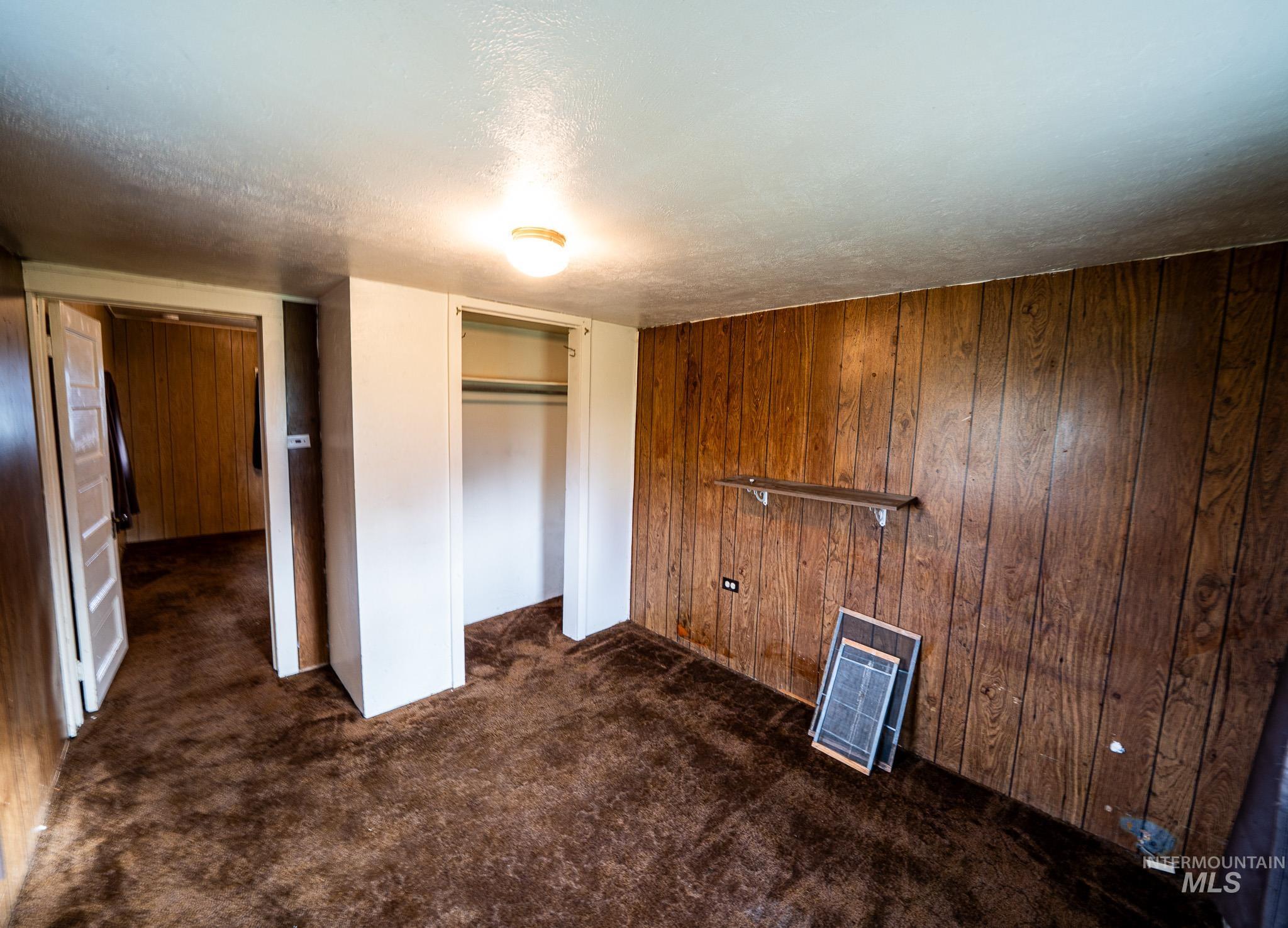 Unfurnished bedroom with a textured ceiling, dark colored carpet, wooden walls, heating unit, and a closet