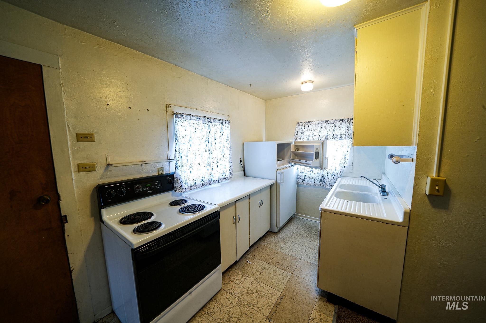 Kitchen featuring electric stove, light countertops, light floors, a textured ceiling, and a textured wall