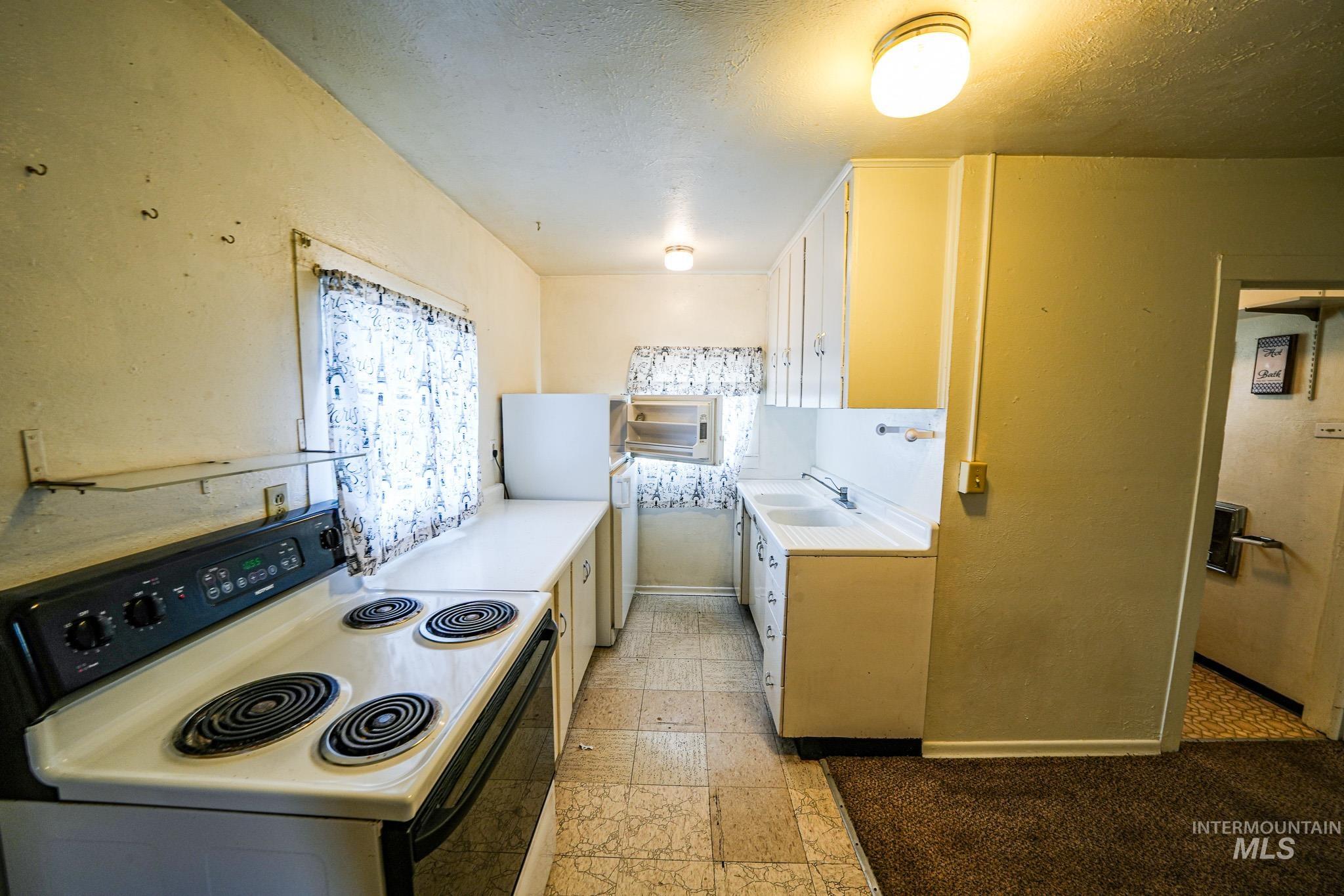 Kitchen with electric range, light countertops, white cabinets, a textured ceiling, and stone tile floors