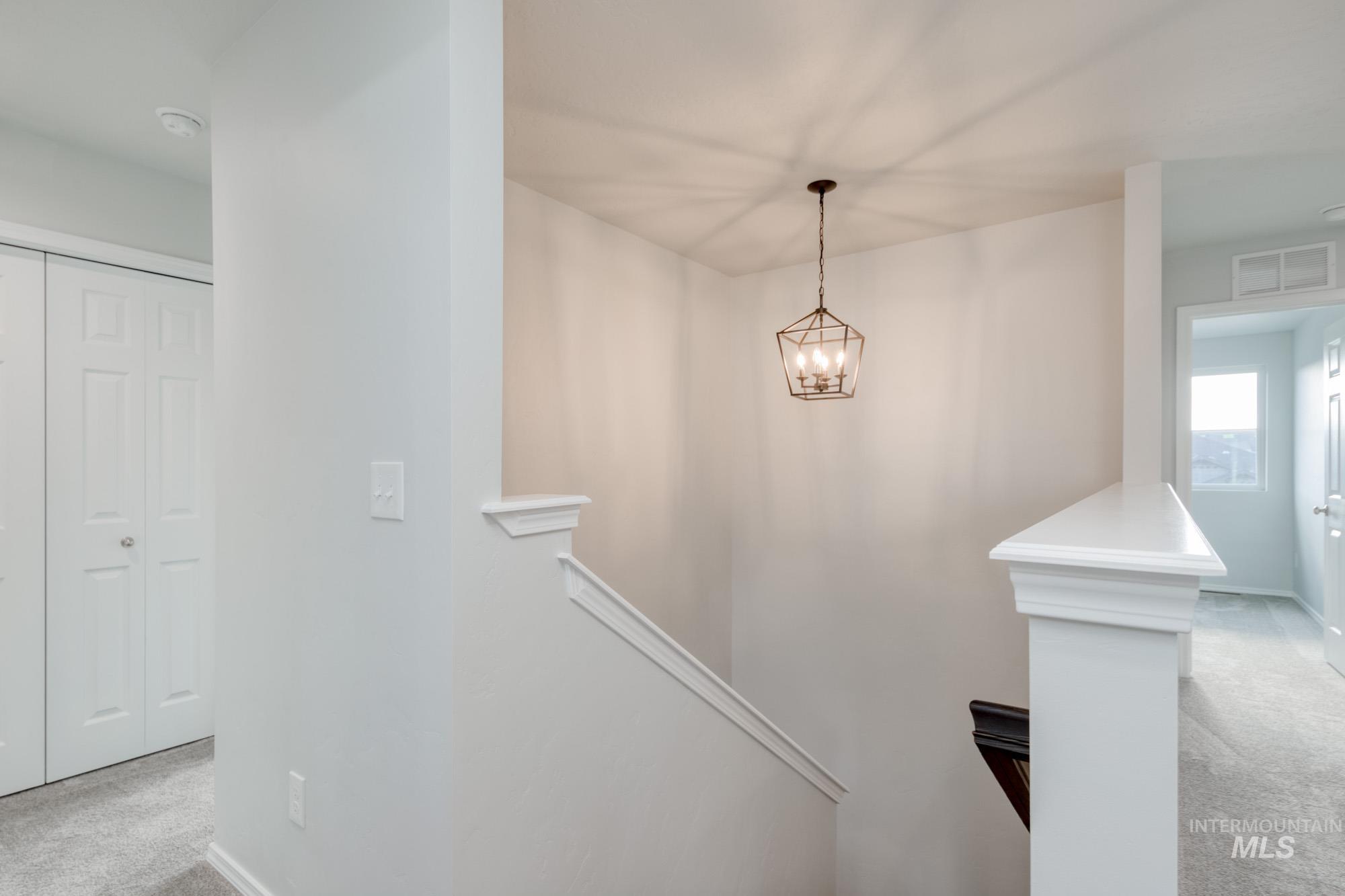 Hallway featuring light carpet, a chandelier, and an upstairs landing