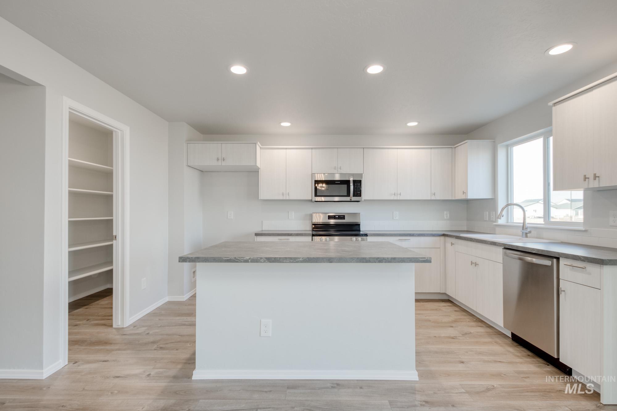 Kitchen featuring stainless steel appliances, white cabinets, recessed lighting, light wood-style flooring, and a kitchen island