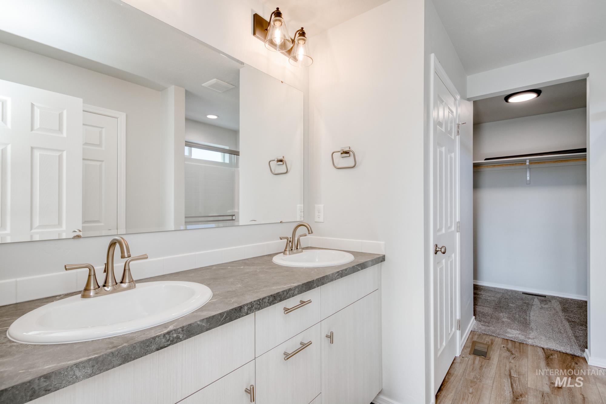 Full bath featuring a walk in closet, double vanity, a shower stall, and light wood finished floors