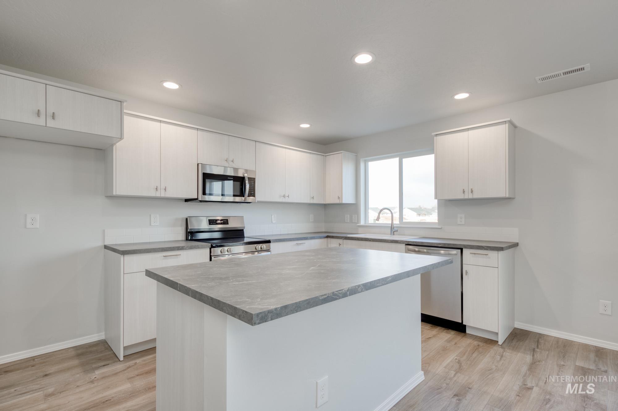 Kitchen with appliances with stainless steel finishes, a kitchen island, light wood-style floors, recessed lighting, and white cabinets