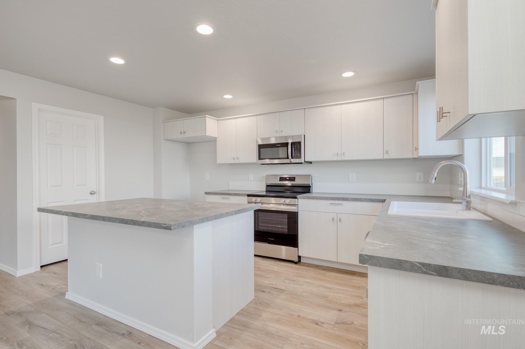 Kitchen with stainless steel appliances, light wood finished floors, recessed lighting, white cabinetry, and a kitchen island