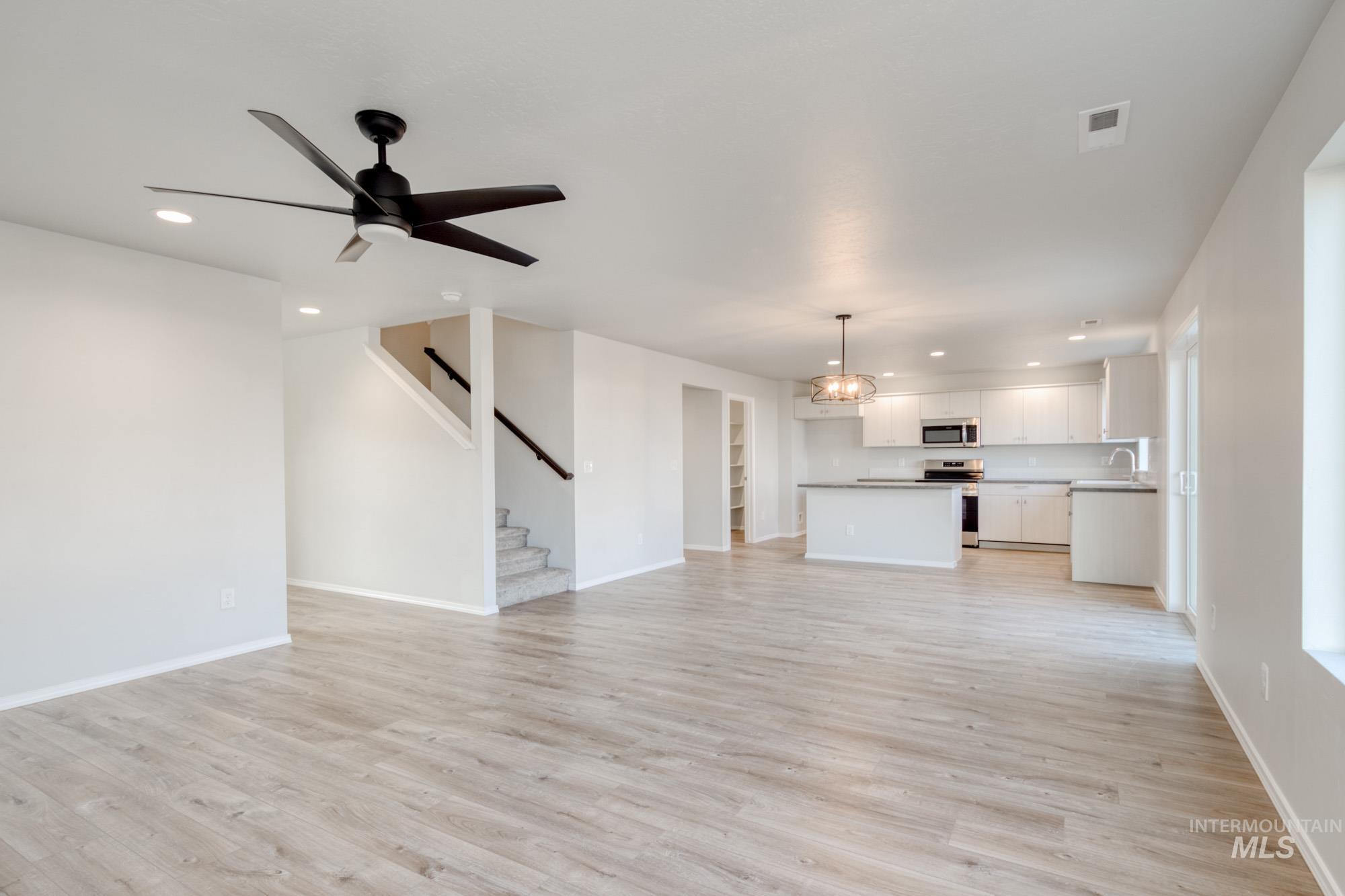 Unfurnished living room featuring recessed lighting, light wood-type flooring, a ceiling fan, and stairway