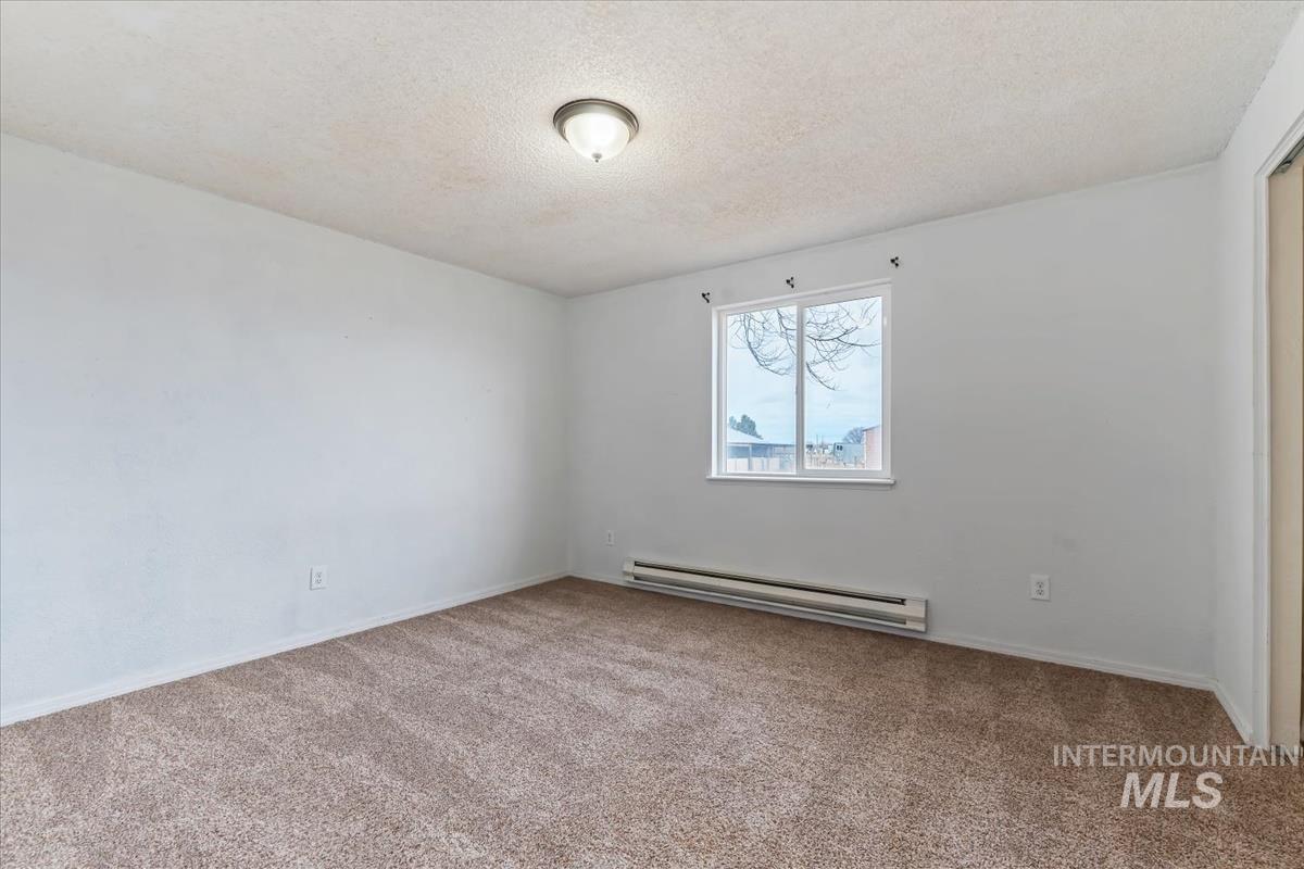 Unfurnished room featuring a textured ceiling, a baseboard radiator, and light carpet