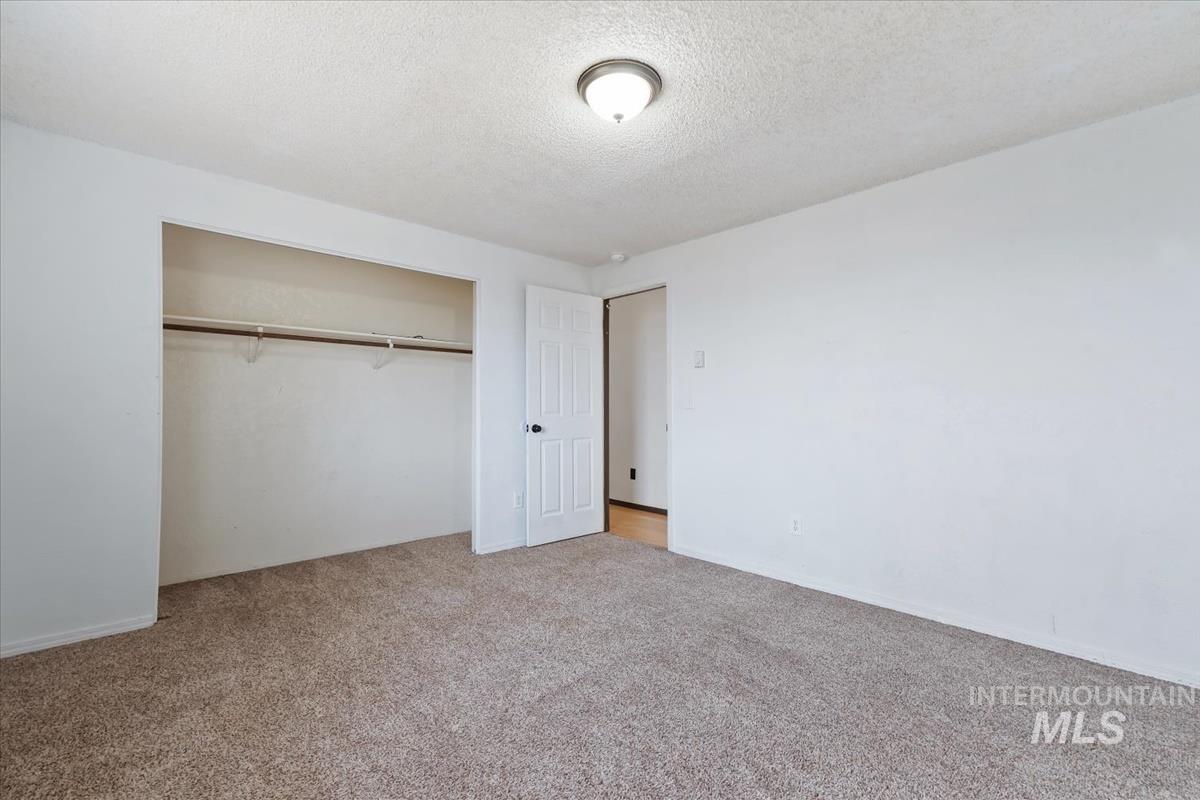 Unfurnished bedroom featuring a textured ceiling, light colored carpet, and a closet