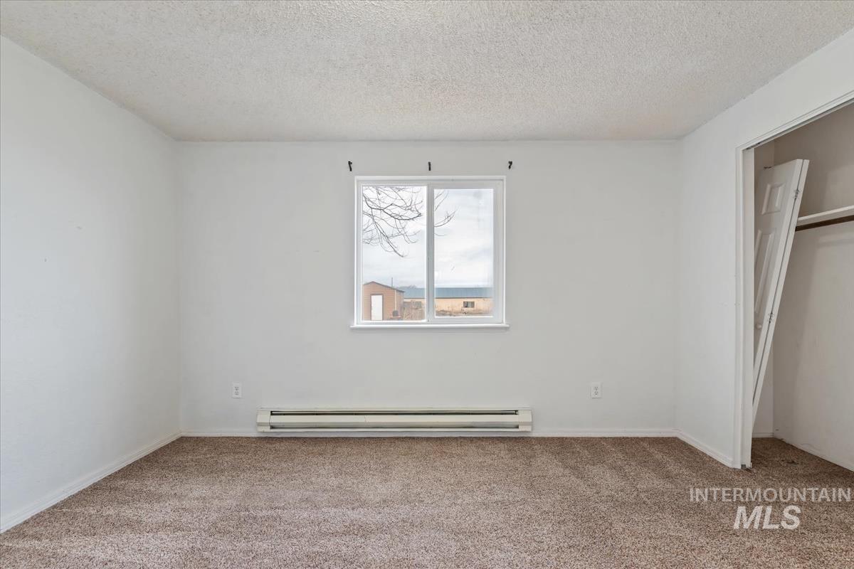 Unfurnished bedroom featuring a textured ceiling, light carpet, a baseboard radiator, and a closet