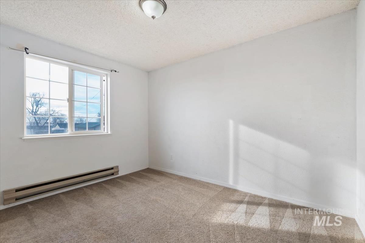 Carpeted spare room with a baseboard heating unit and a textured ceiling