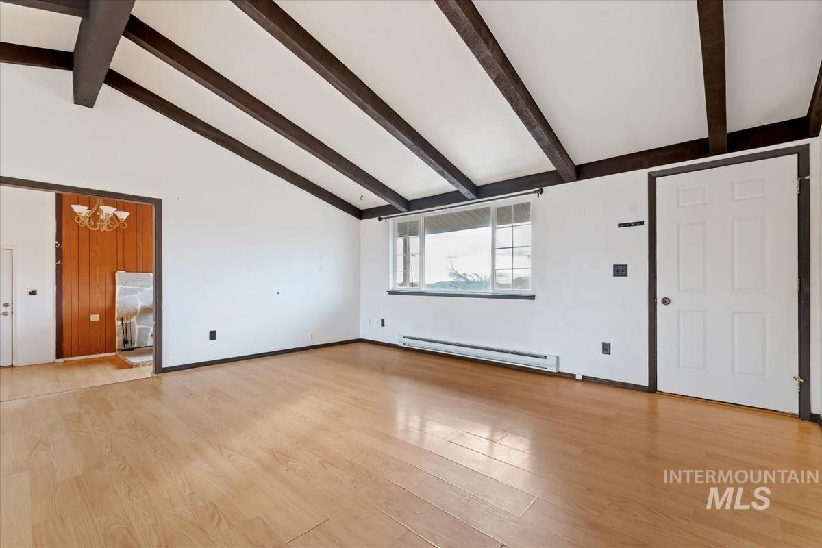 Unfurnished living room with a chandelier, light wood finished floors, a baseboard heating unit, beam ceiling, and high vaulted ceiling