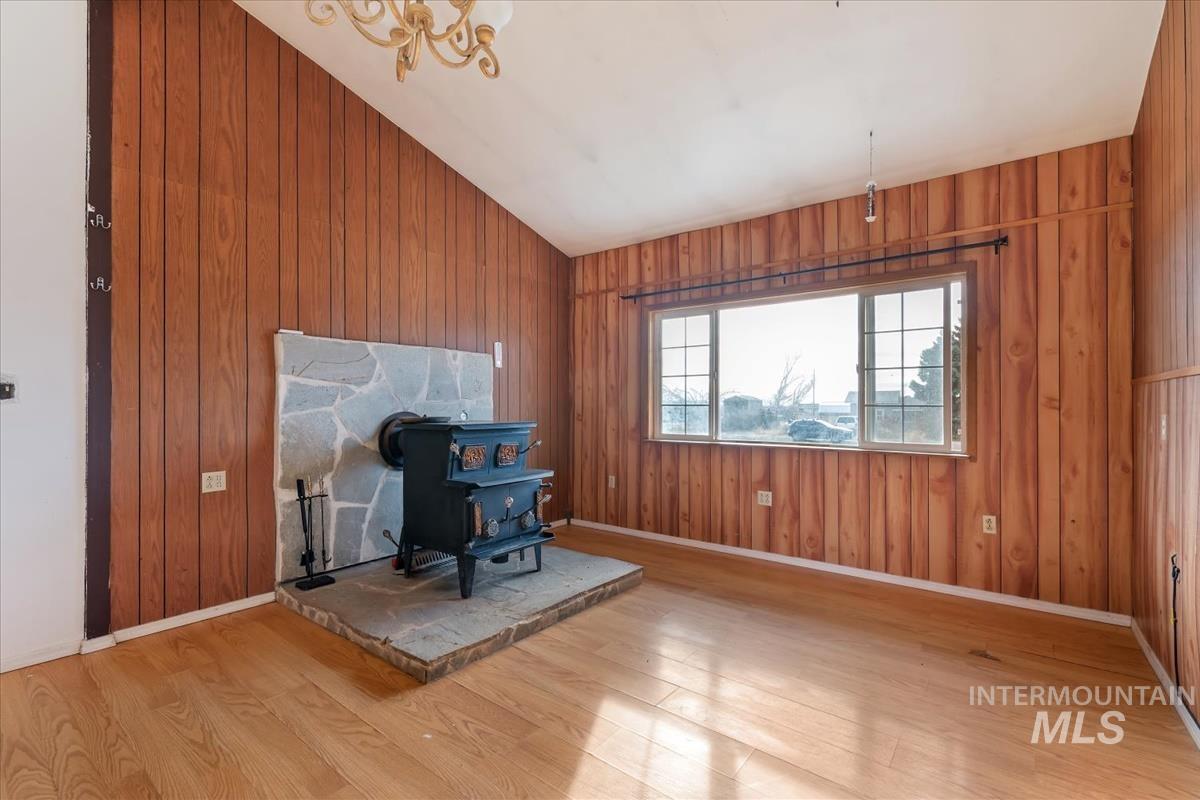 Unfurnished living room featuring a wood stove, lofted ceiling, light wood-type flooring, and wood walls