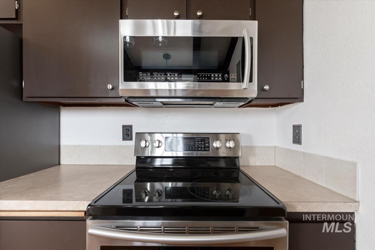 Kitchen with stainless steel appliances, light countertops, and dark brown cabinets