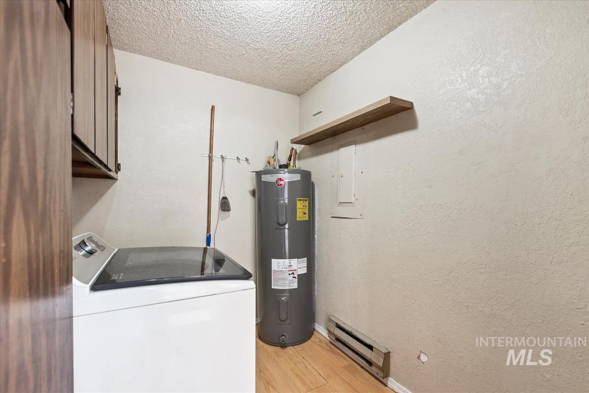 Washroom featuring washer / clothes dryer, baseboard heating, a textured ceiling, electric water heater, and cabinet space