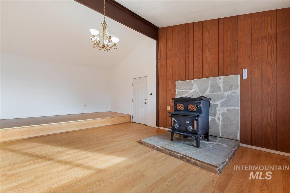 Unfurnished living room with a wood stove, beamed ceiling, light wood-type flooring, wooden walls, and a chandelier