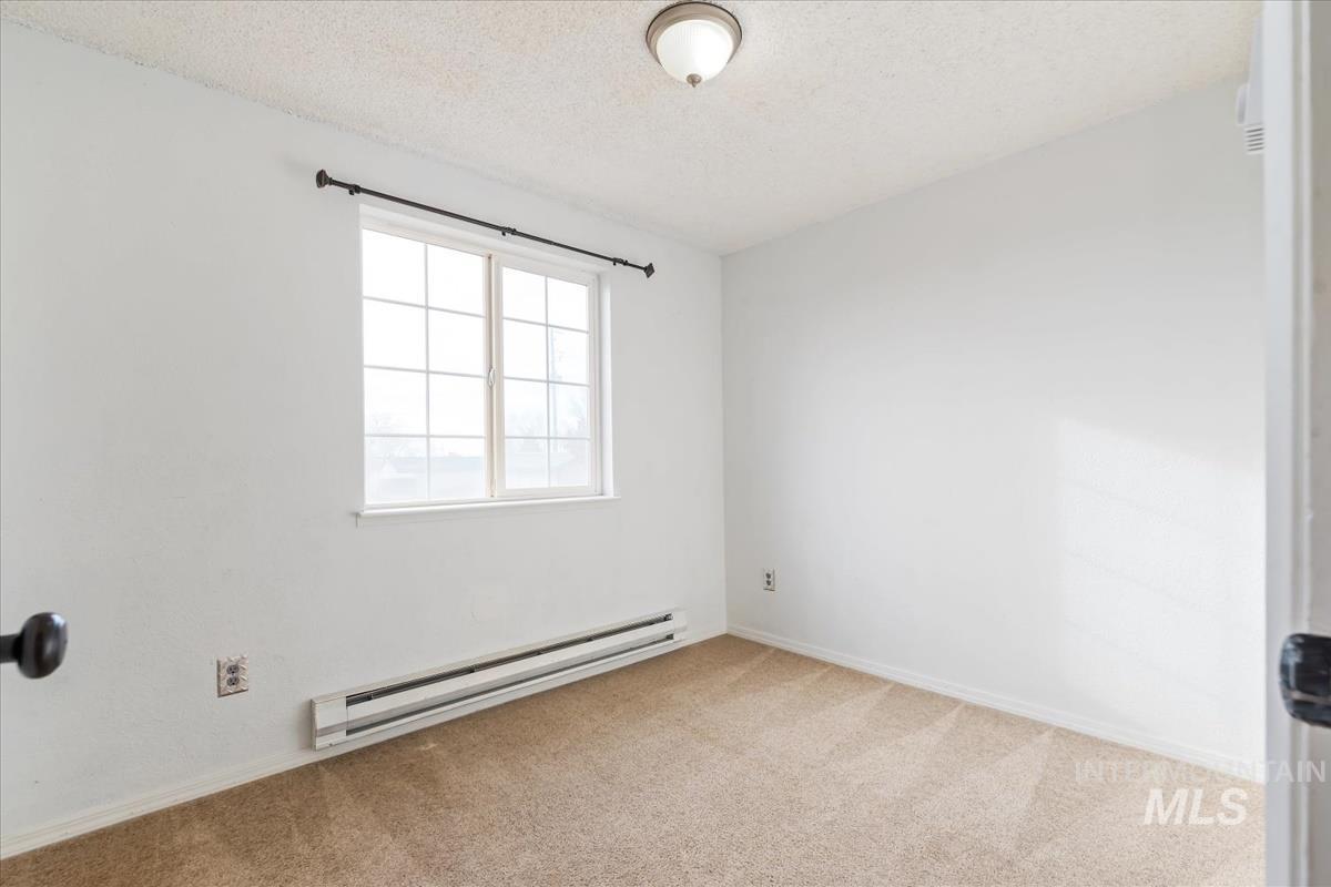 Carpeted empty room with a textured ceiling and a baseboard heating unit