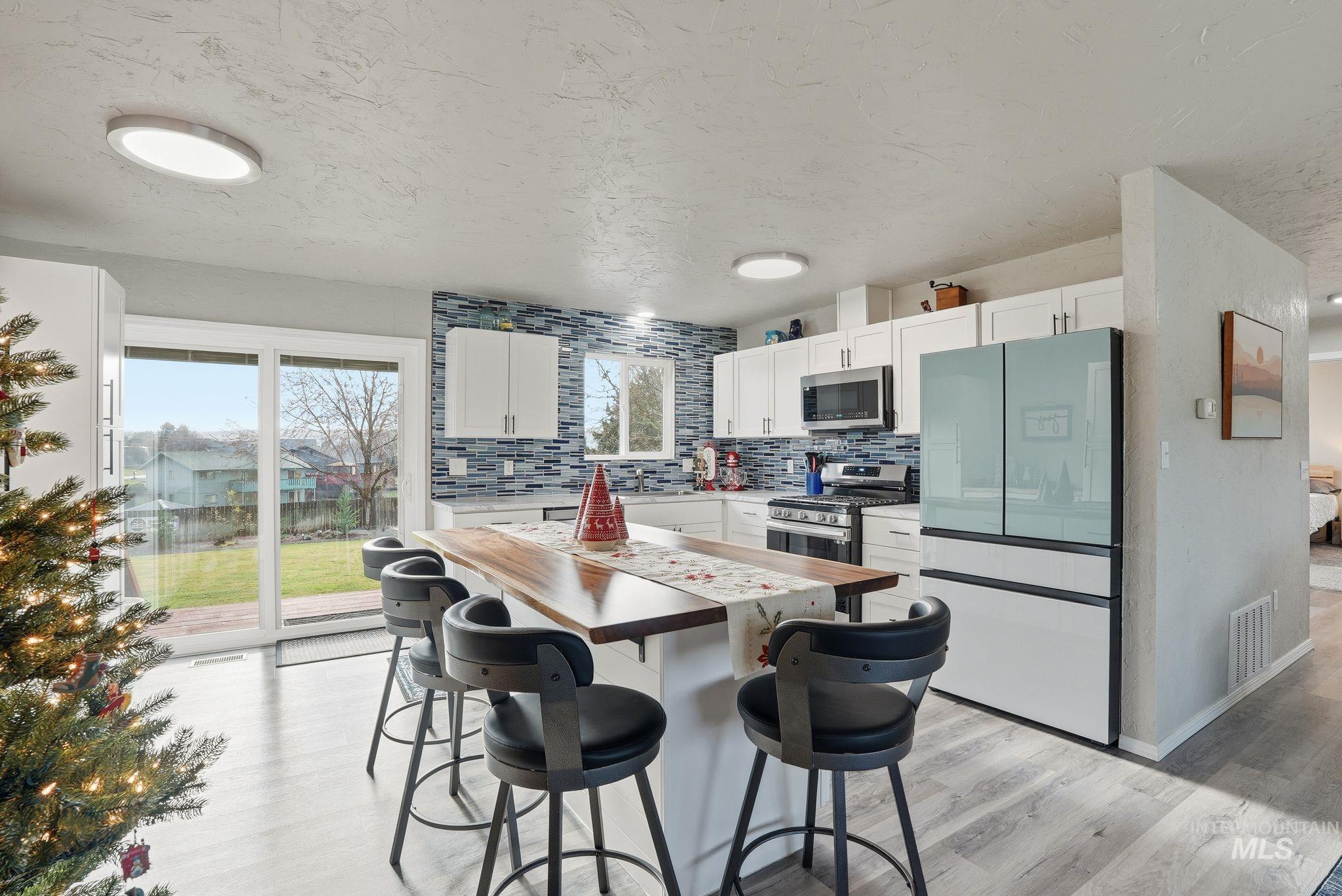 Kitchen with butcher block countertops, freestanding refrigerator, white cabinets, a kitchen breakfast bar, and light wood-style flooring