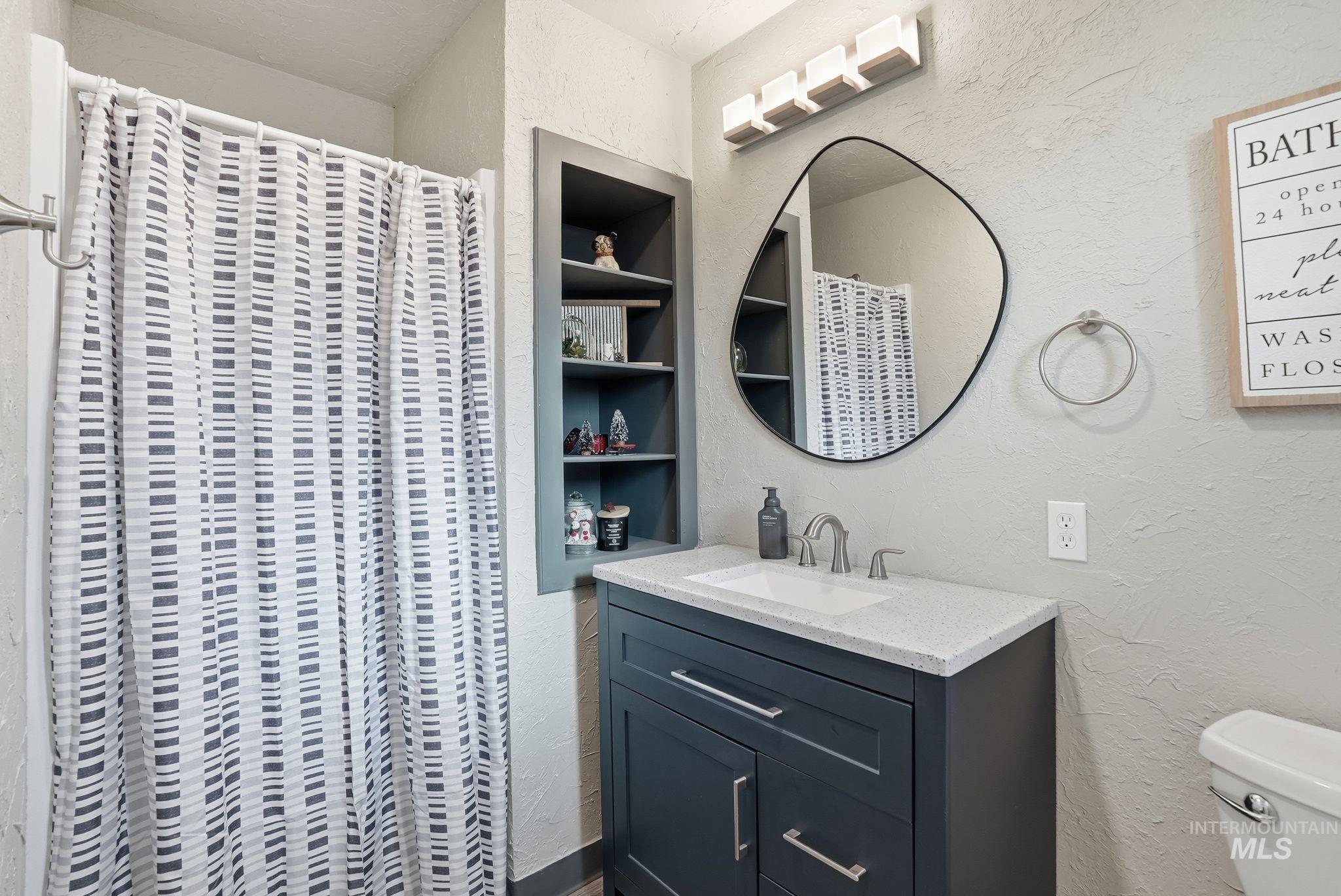 Bathroom with a textured wall, vanity, curtained shower, and built in shelves