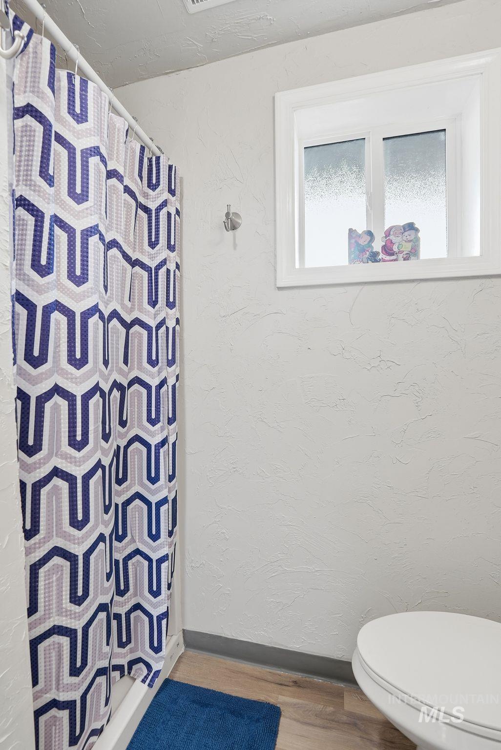 Bathroom featuring a shower with curtain, a textured wall, and wood finished floors