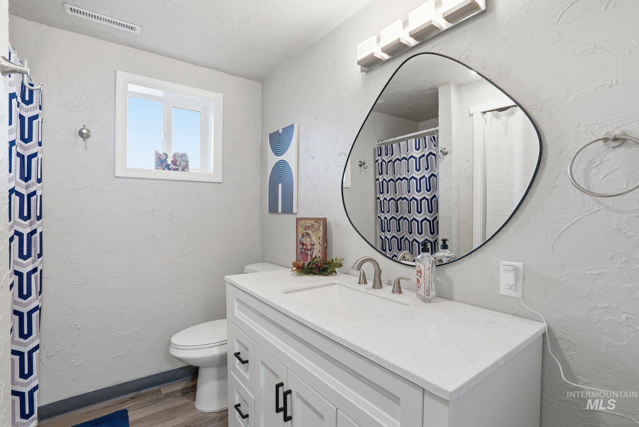 Bathroom with a textured wall, vanity, a shower with shower curtain, and light wood-style floors
