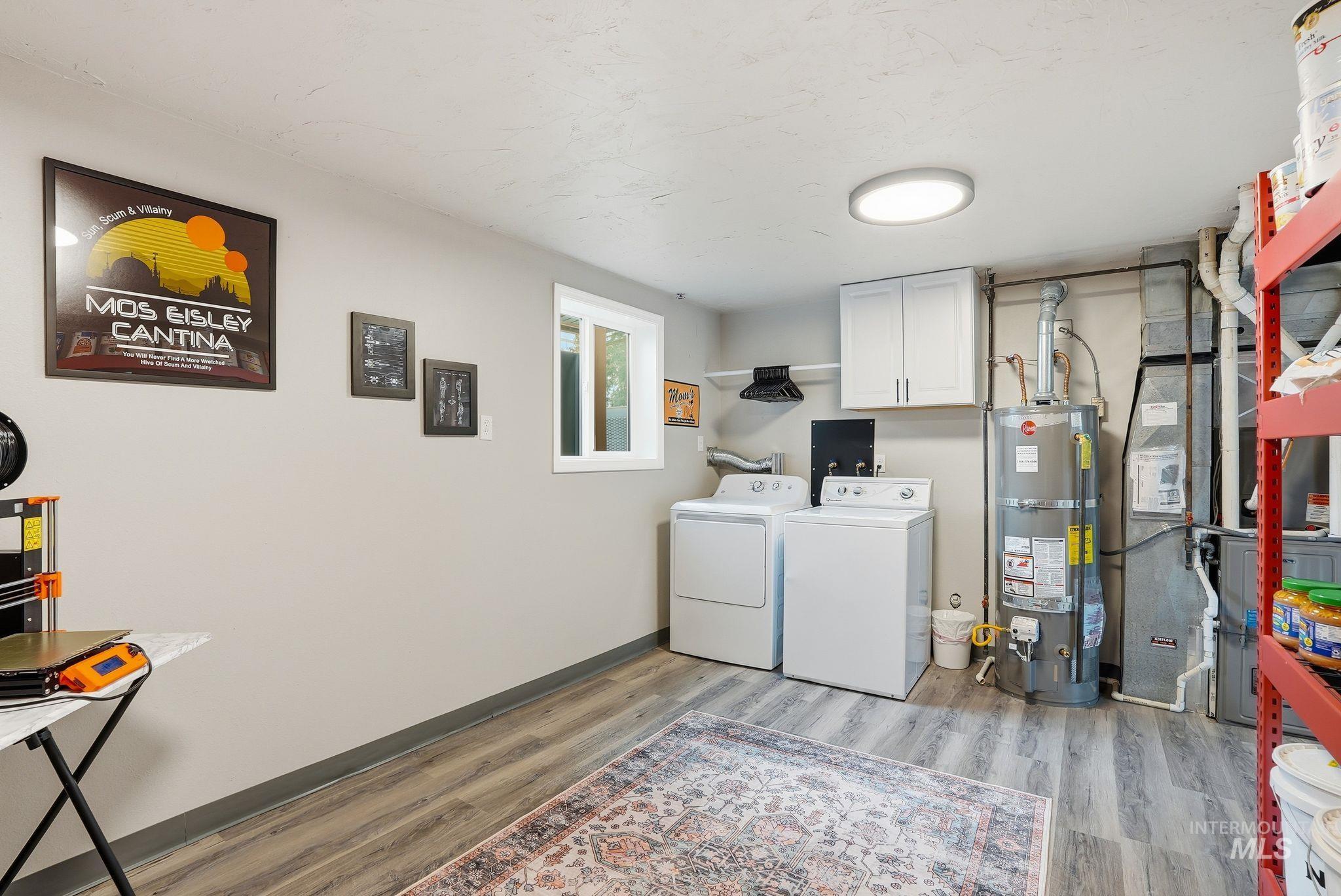 Washroom with cabinet space, washer and dryer, strapped water heater, and light wood finished floors