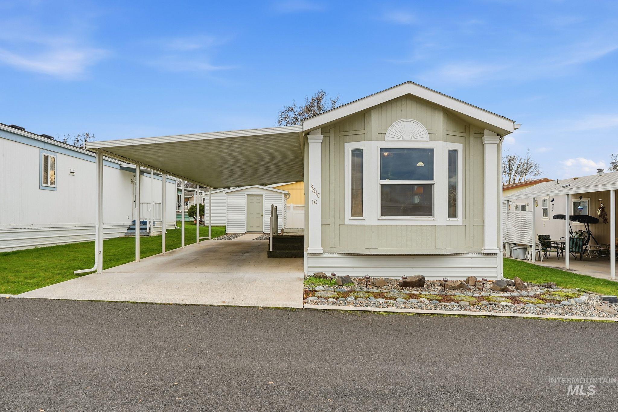 Manufactured / mobile home featuring an attached carport, driveway, and an outdoor structure