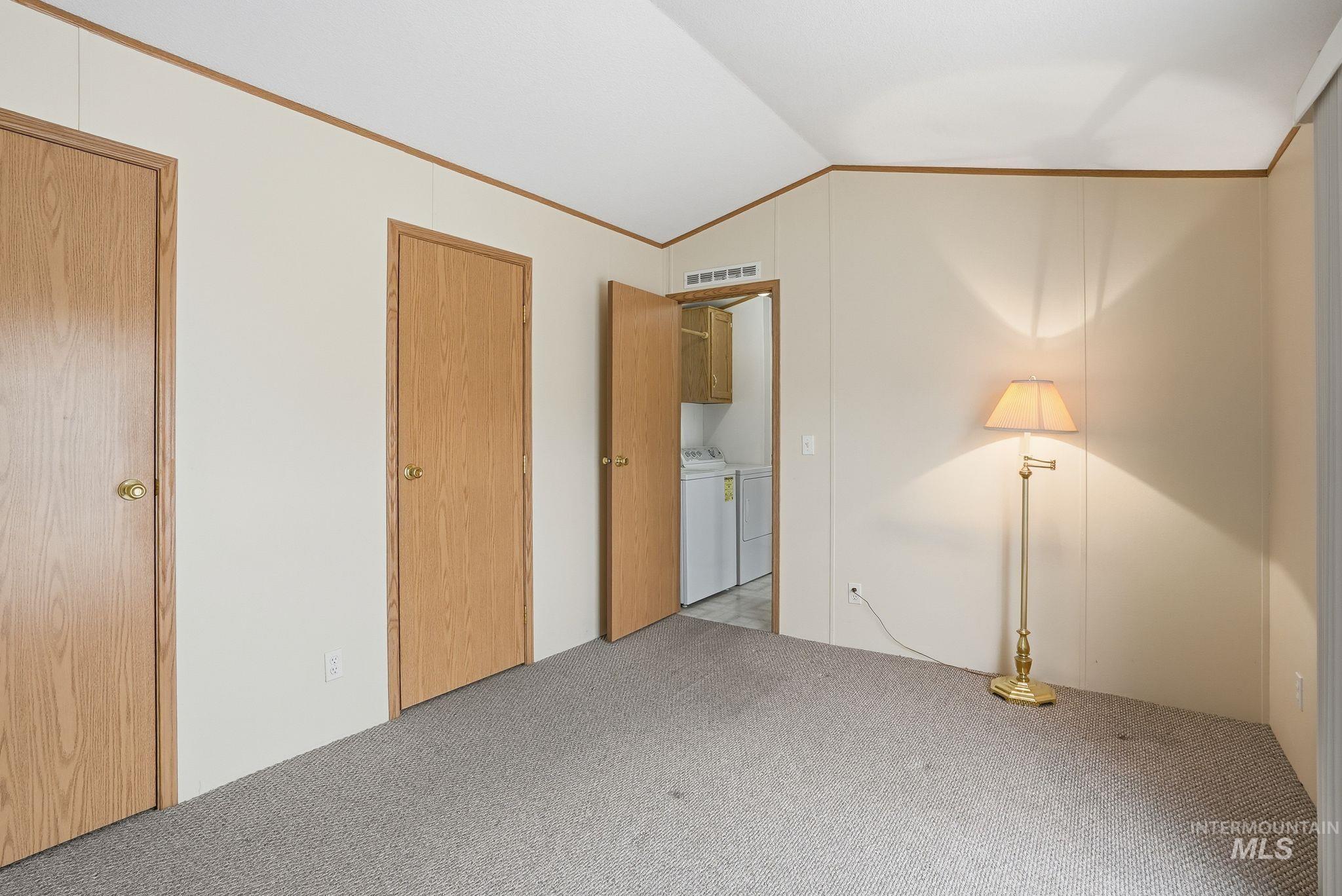 Unfurnished bedroom with lofted ceiling, carpet floors, washer and dryer, and ornamental molding