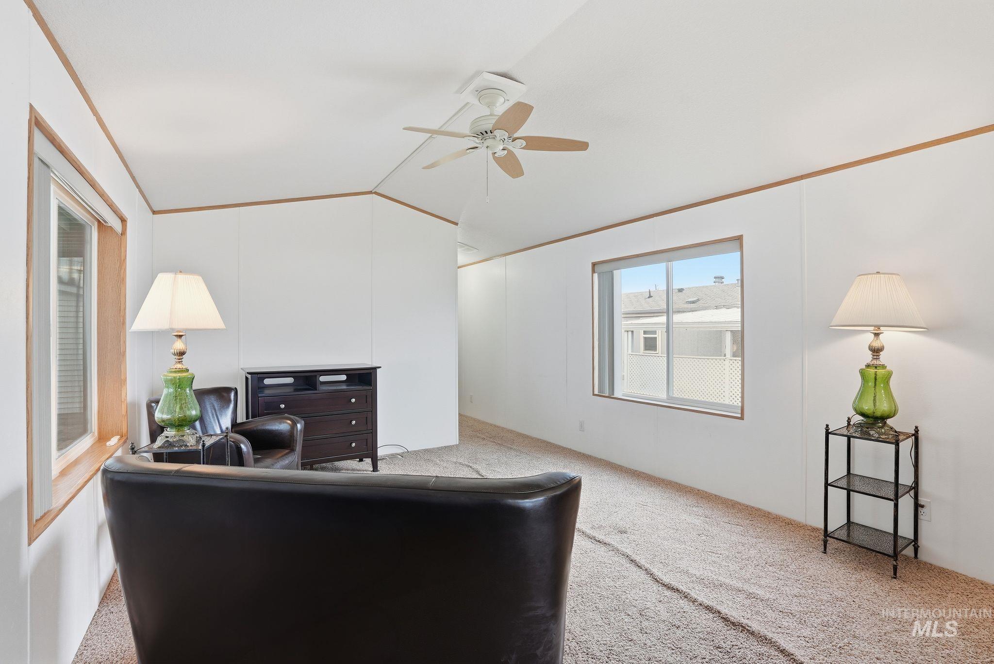 Carpeted living area with vaulted ceiling, crown molding, and ceiling fan