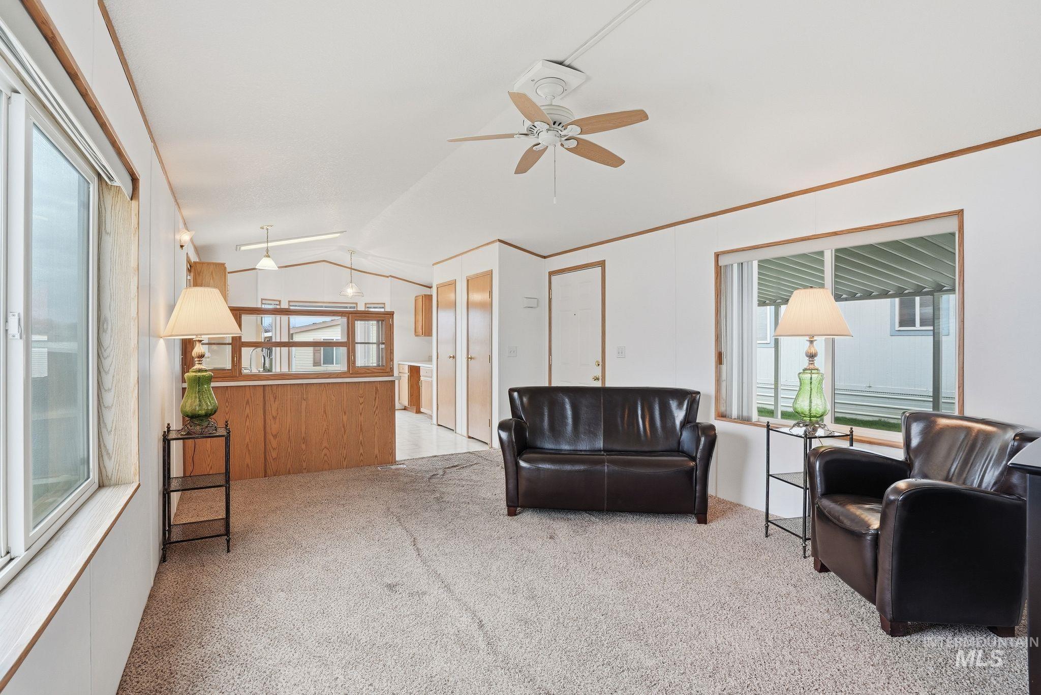 Living room featuring plenty of natural light, light colored carpet, lofted ceiling, and ceiling fan