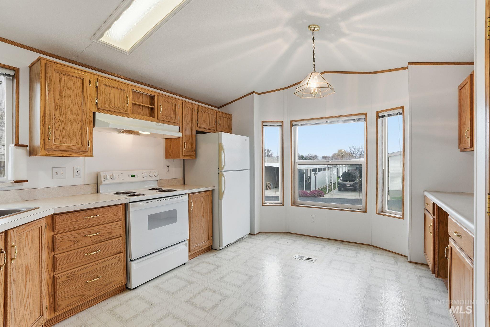 Kitchen with light floors, white appliances, light countertops, under cabinet range hood, and ornamental molding