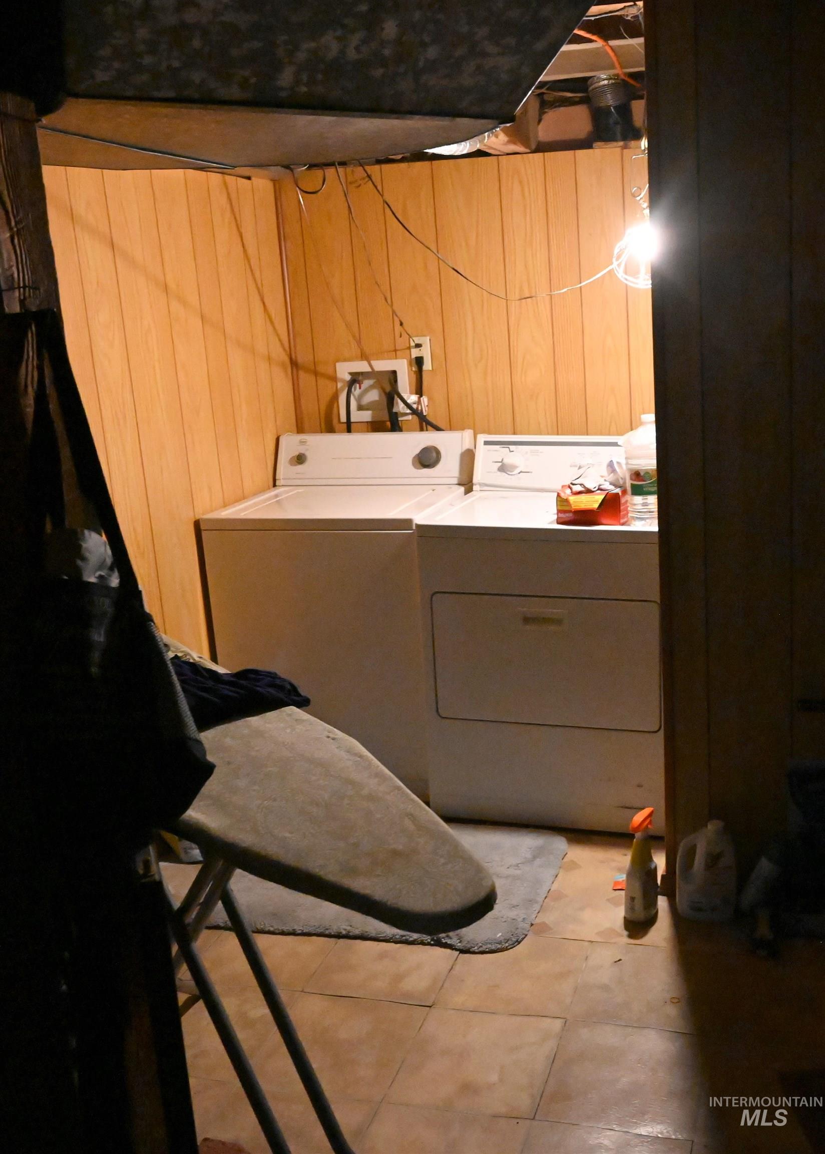 Laundry room with wooden walls, light tile patterned floors, and washer and dryer