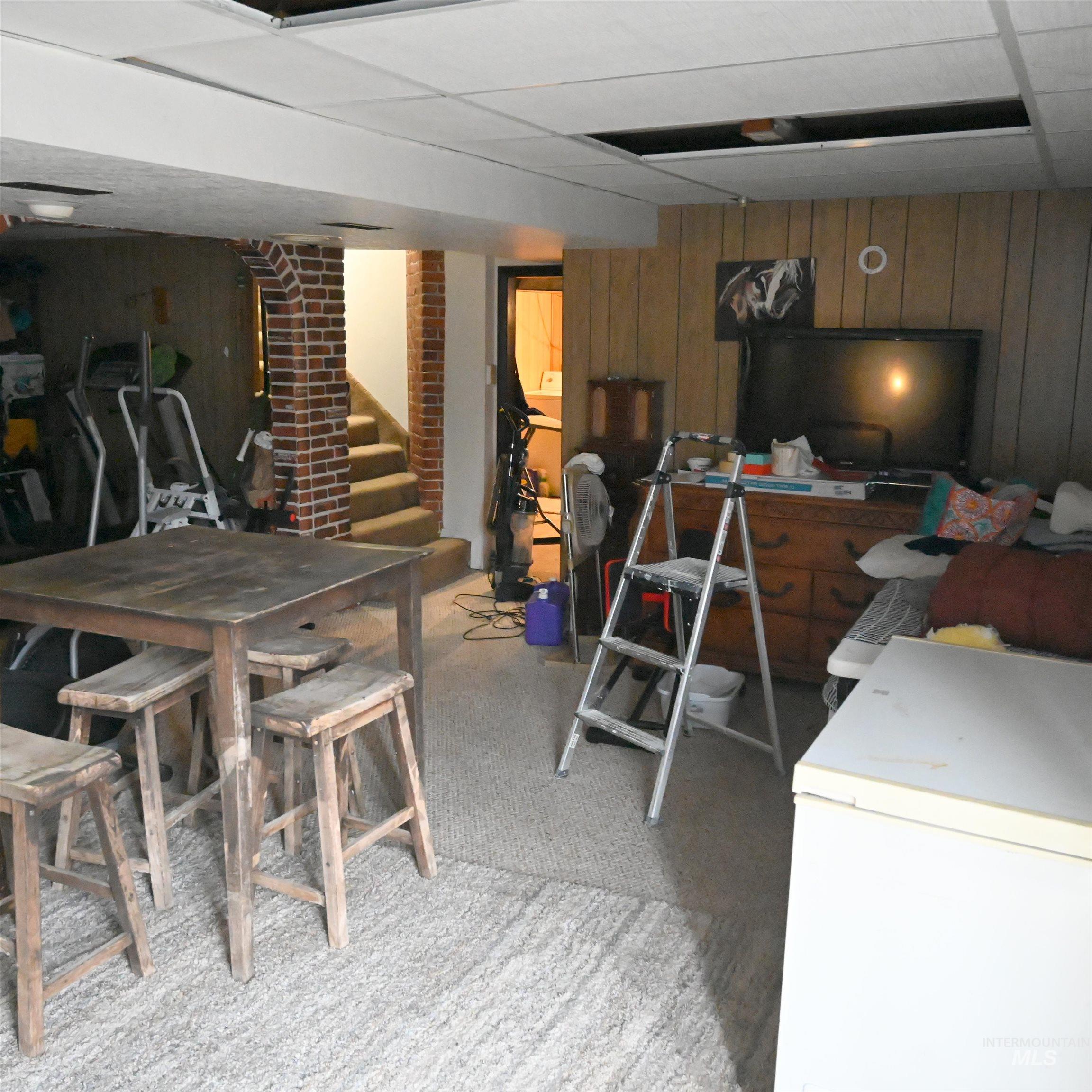 Finished basement with wood walls, white refrigerator, stairway, light carpet, and a paneled ceiling