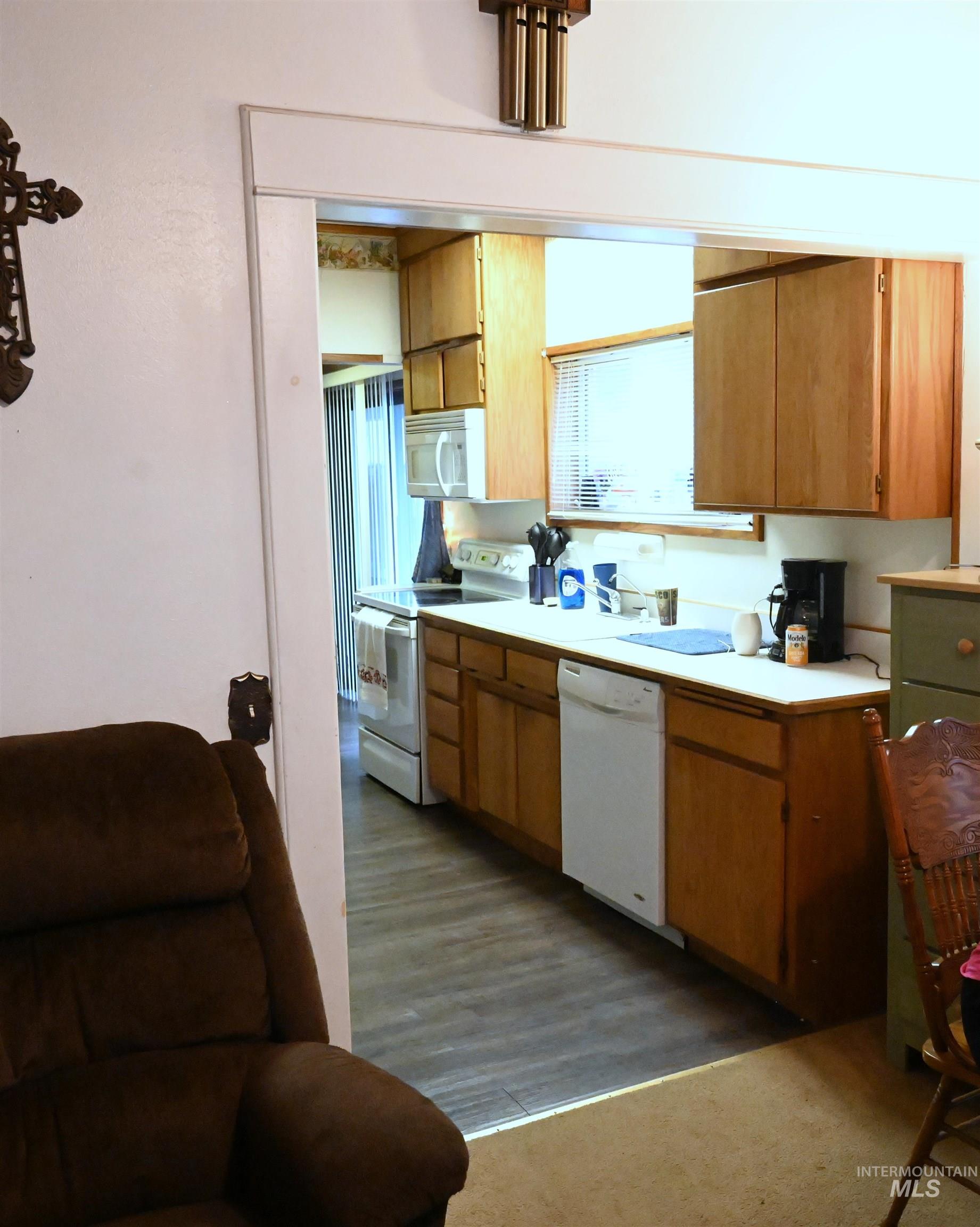 Kitchen with light countertops, white appliances, brown cabinetry, and dark wood-style flooring