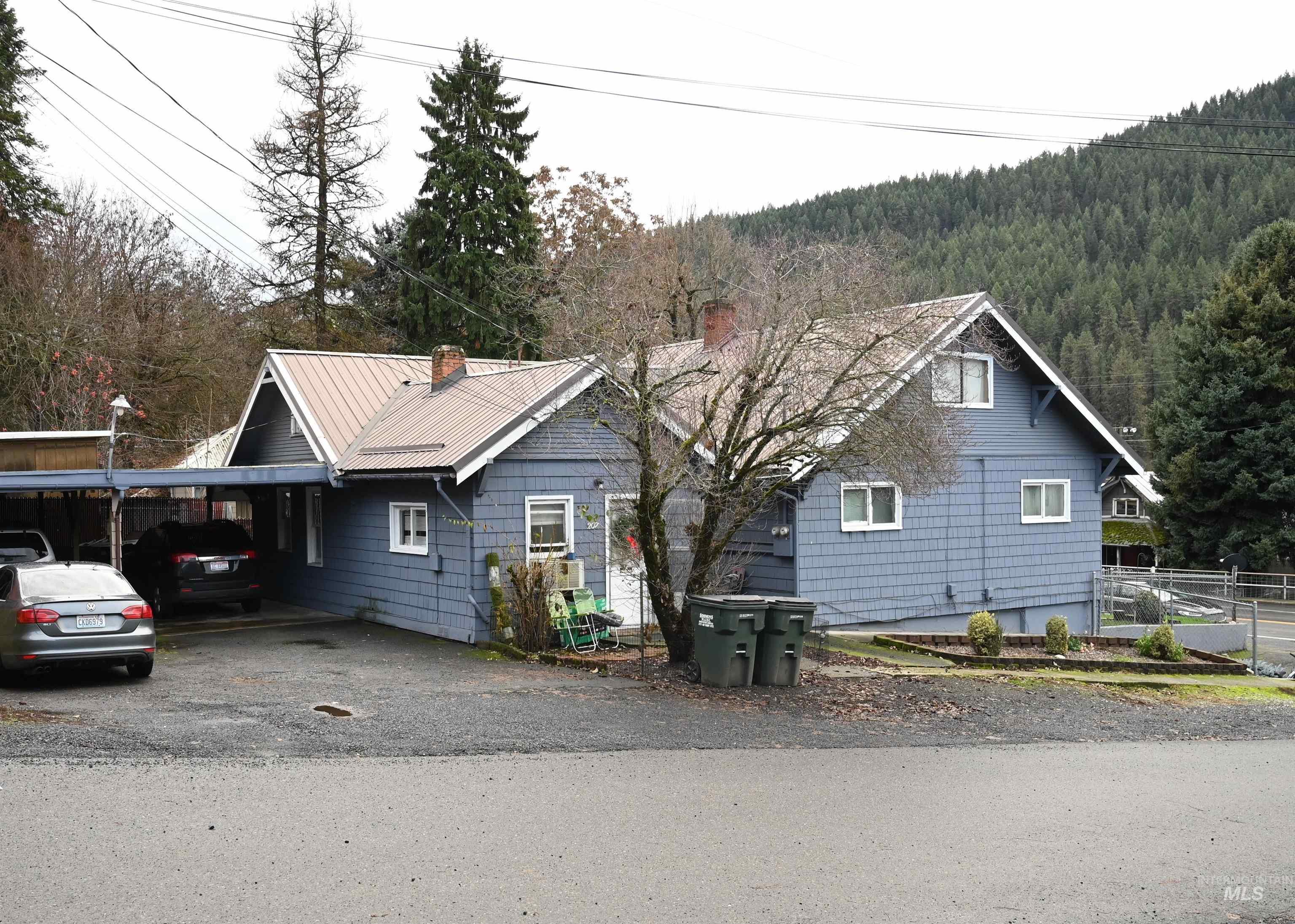 Chalet / cabin featuring a chimney, an attached carport, a metal roof, a view of trees, and driveway
