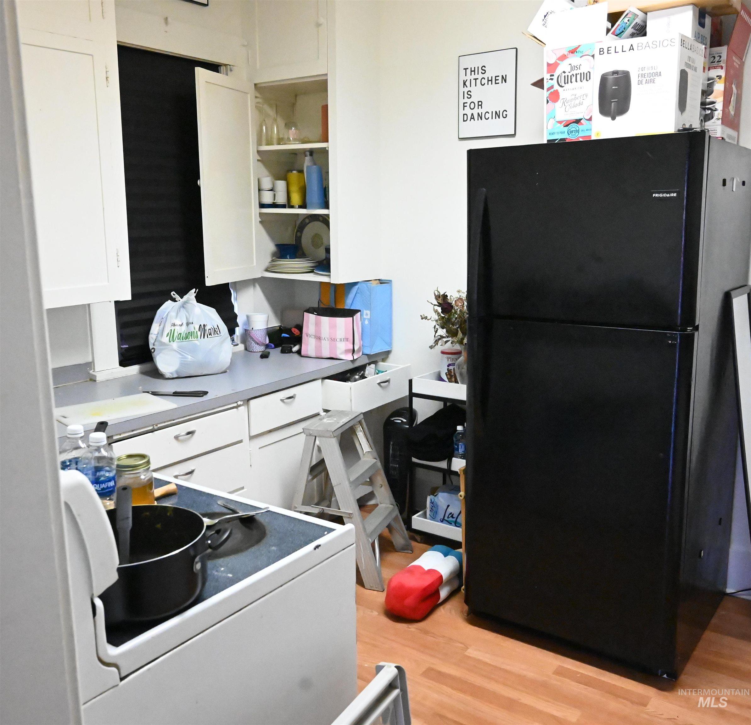 Kitchen featuring freestanding refrigerator, white cabinets, light countertops, open shelves, and light wood-style flooring