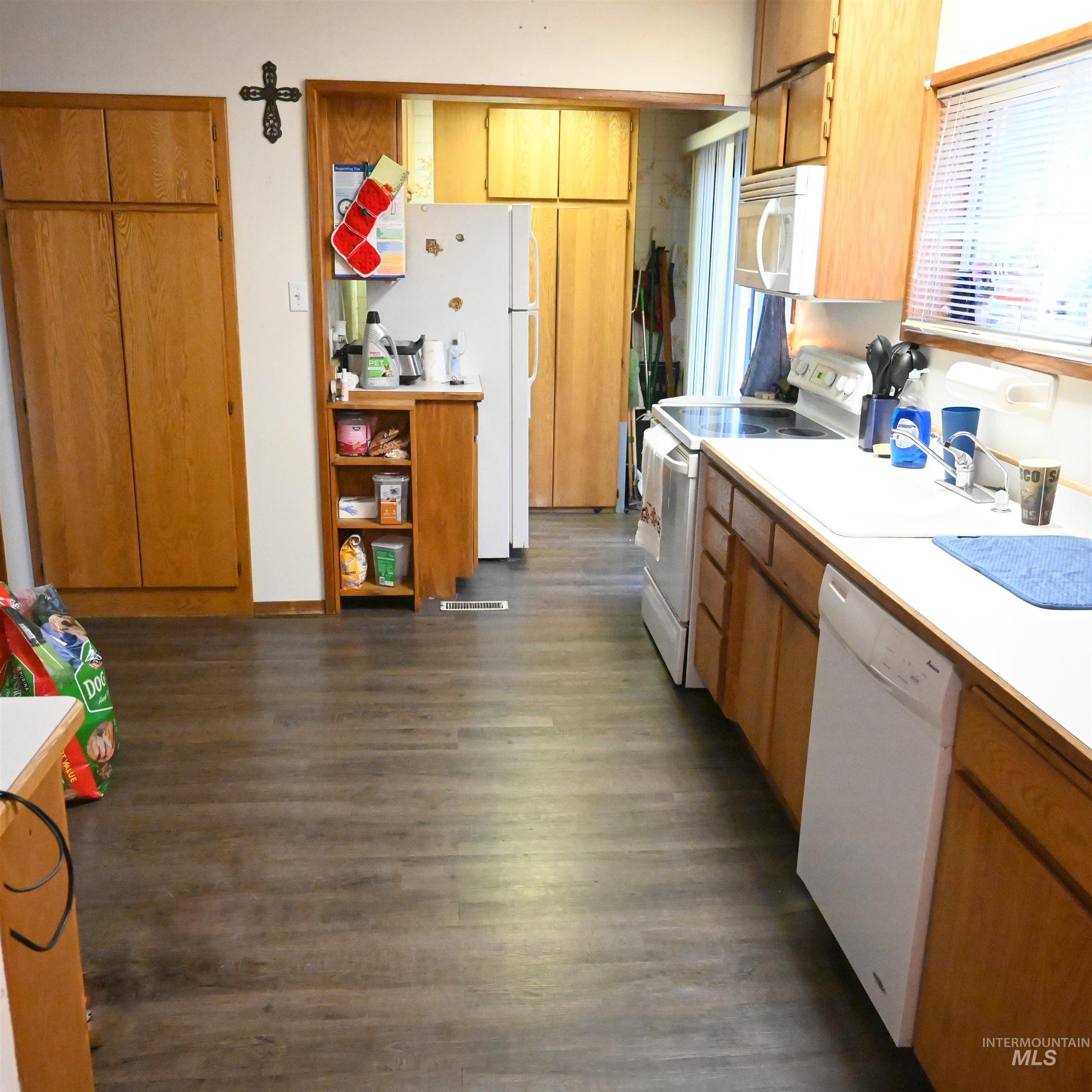 Kitchen with white appliances, light countertops, brown cabinets, and dark wood-style floors