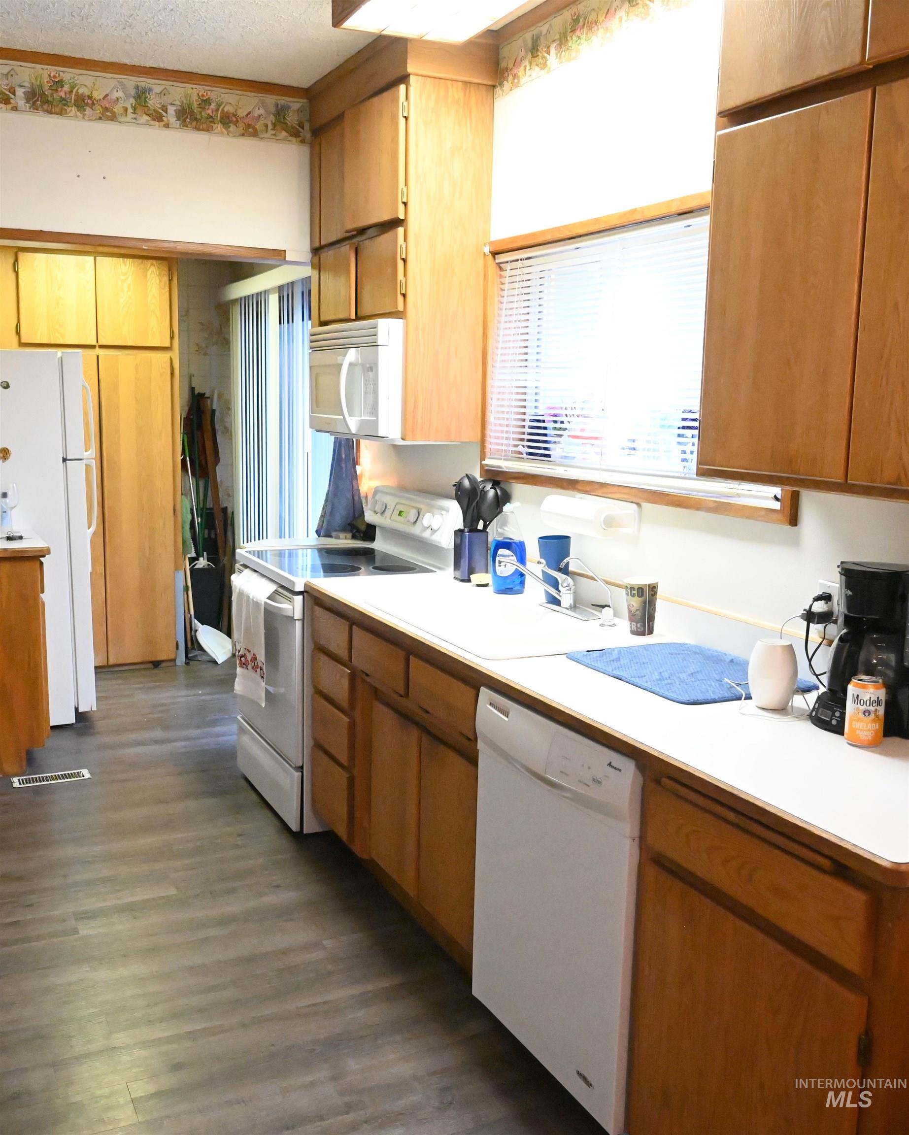 Kitchen featuring light countertops, white appliances, brown cabinets, a textured ceiling, and dark wood-style floors