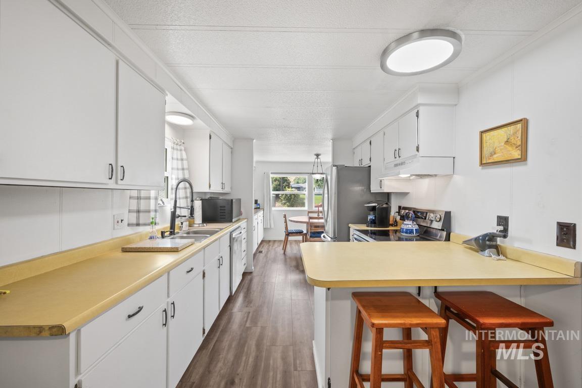Kitchen with a kitchen bar, a peninsula, light countertops, dark wood finished floors, and stainless steel appliances