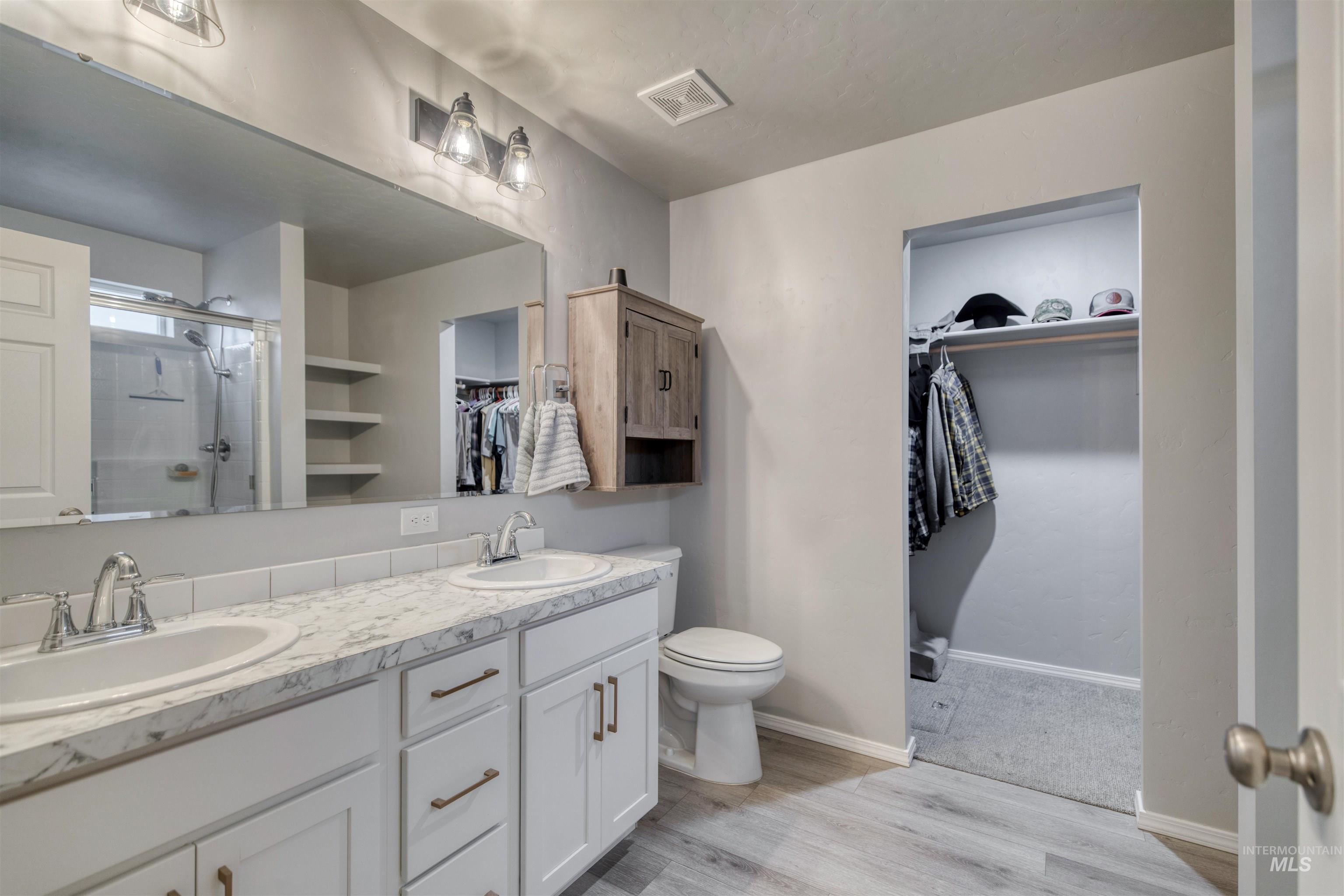 Bathroom with a walk in closet, a stall shower, double vanity, and light wood-type flooring