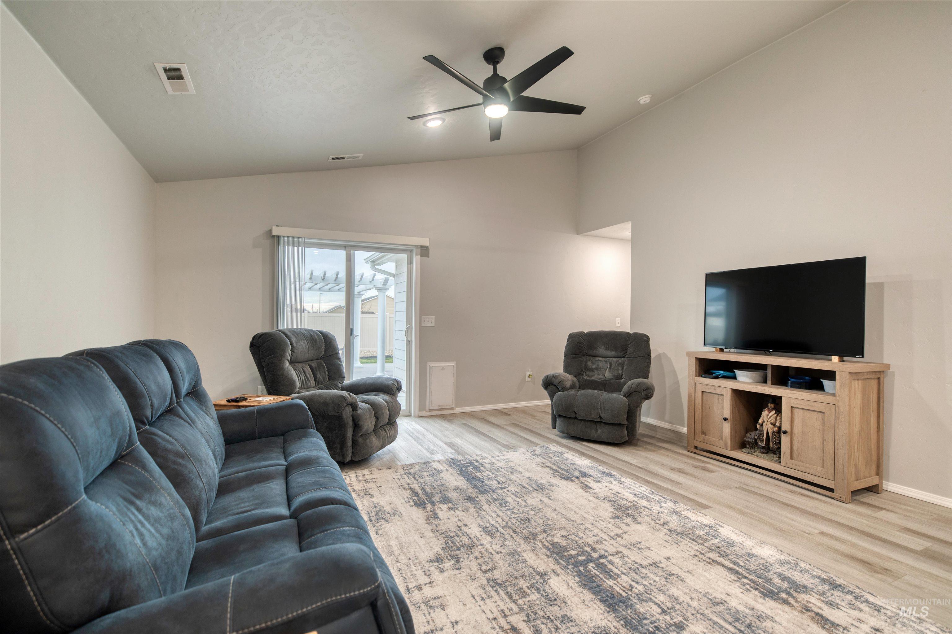Living room featuring vaulted ceiling, light wood-style floors, and ceiling fan